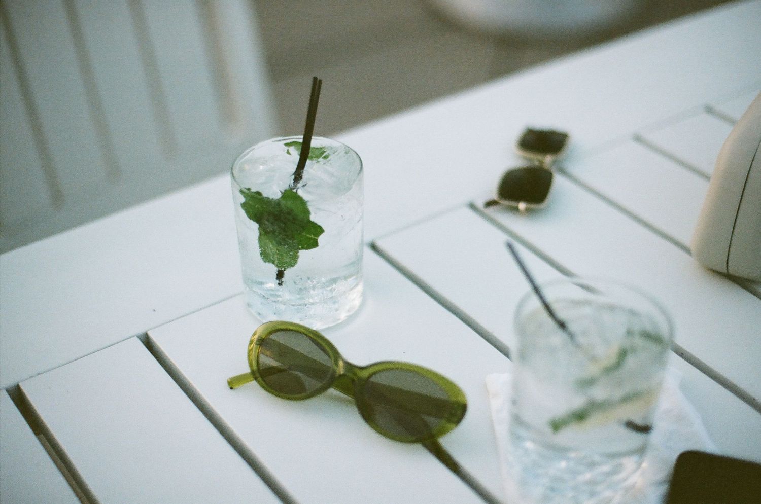 Retro sunglasses and mojito cocktails on a white table with fresh mint leaves and ice.