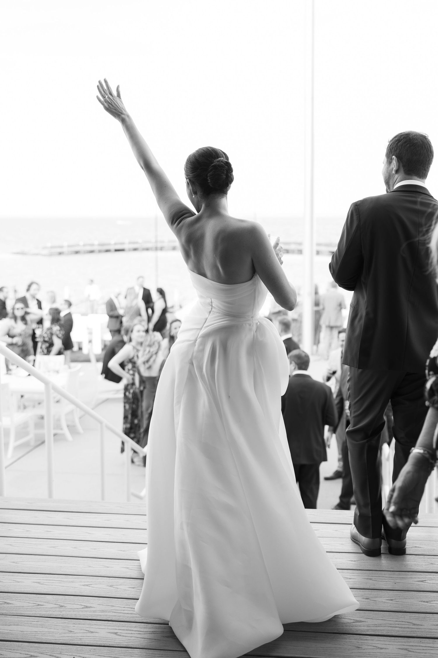 Wedding guests stand and wave from a wooden deck during an outdoor ceremony while overlooking a scenic view.