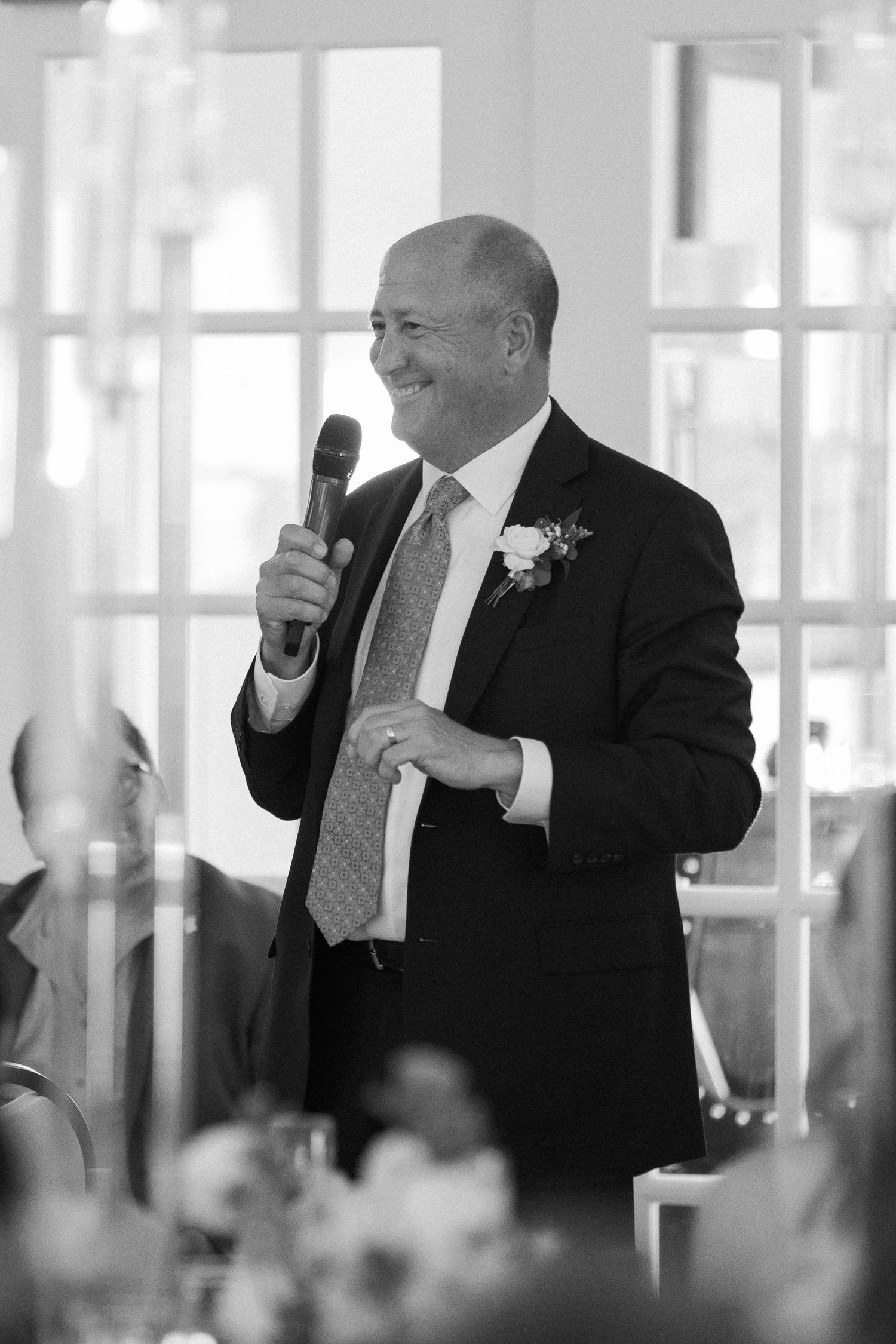 Black and white photo of wedding guests holding up glasses during a formal toast at an elegant reception hall.