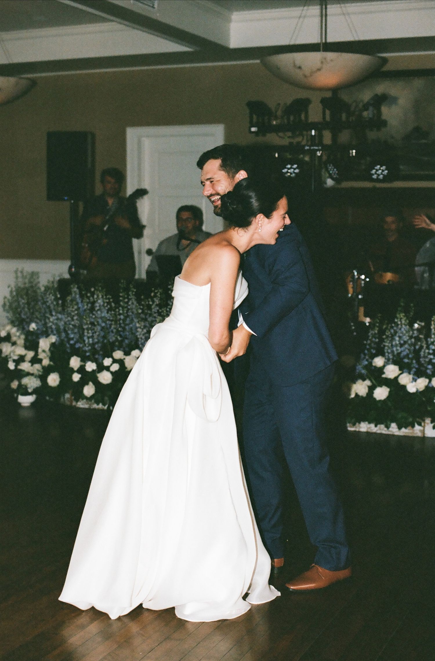 Couple shares a romantic dance moment at wedding reception where bride wears white dress and groom wears navy suit.