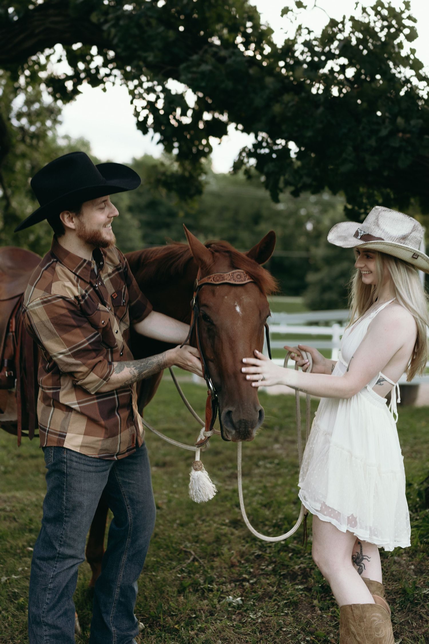 A rustic country engagement photo shoot features a couple and a horse in a pastoral outdoor setting.