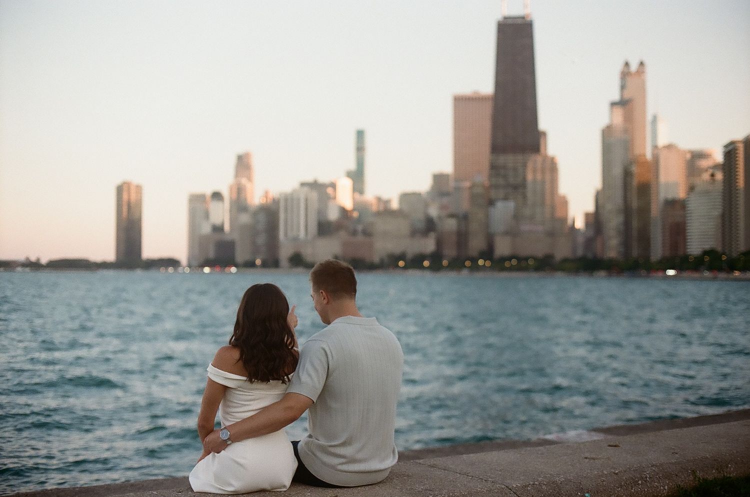 A couple sits together along Lake Michigan enjoying the stunning Chicago skyline view at sunset.