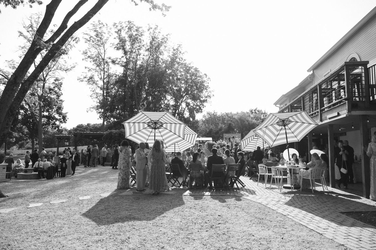 Outdoor patio dining area with striped umbrellas and guests seated at tables near a building.