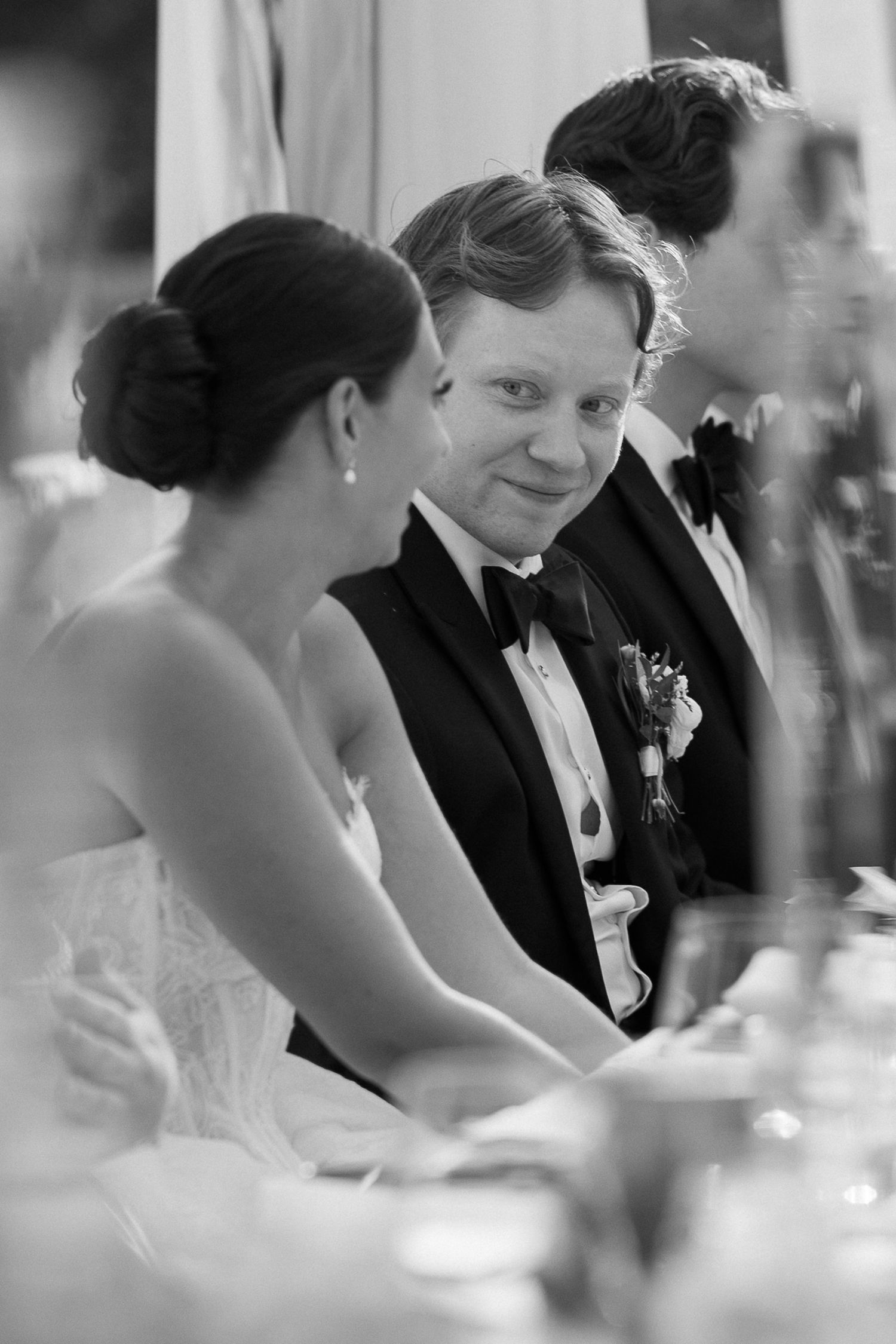 Black and white wedding photo of bride and groom sharing an intimate moment at the reception dinner table.