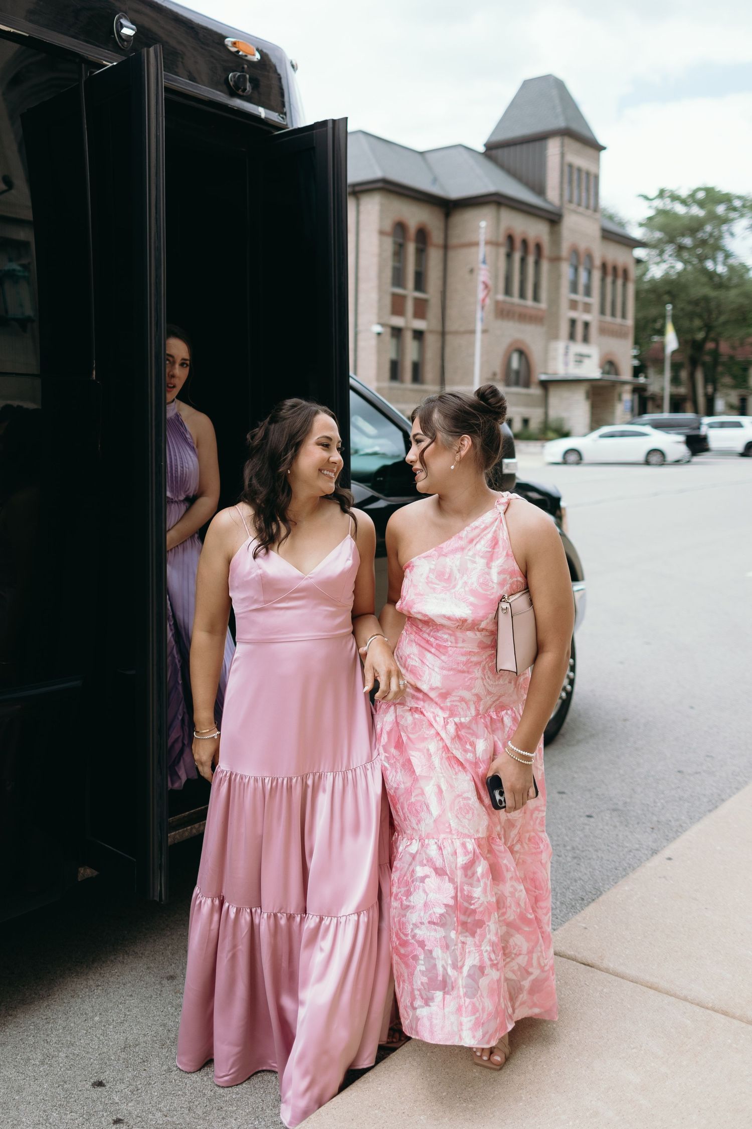 Wedding party members in pink dresses stand outside a church building.