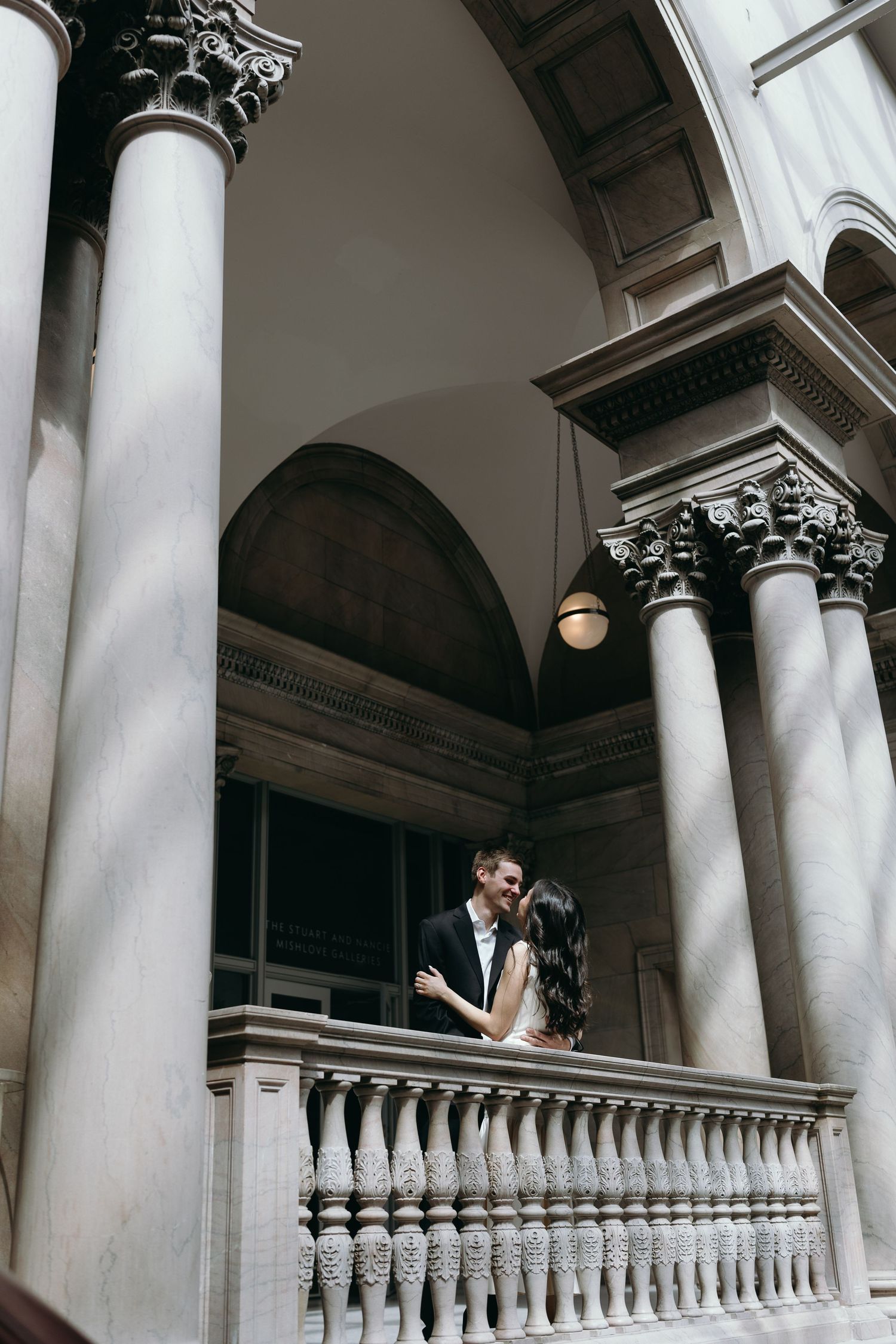 A romantic moment captured on a classical balcony with ornate columns and architecture. The Chicago Art institute engagement inspiration