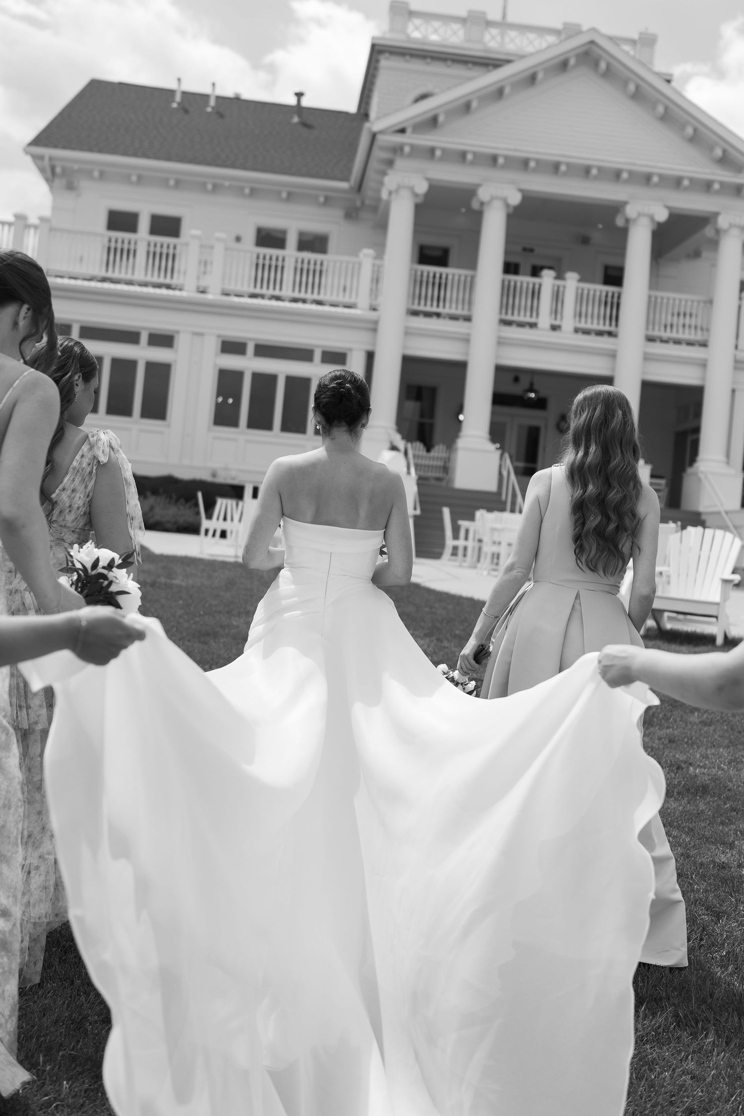 A stunning black and white photo of a wedding dress flowing in the breeze outside an elegant colonial-style mansion.