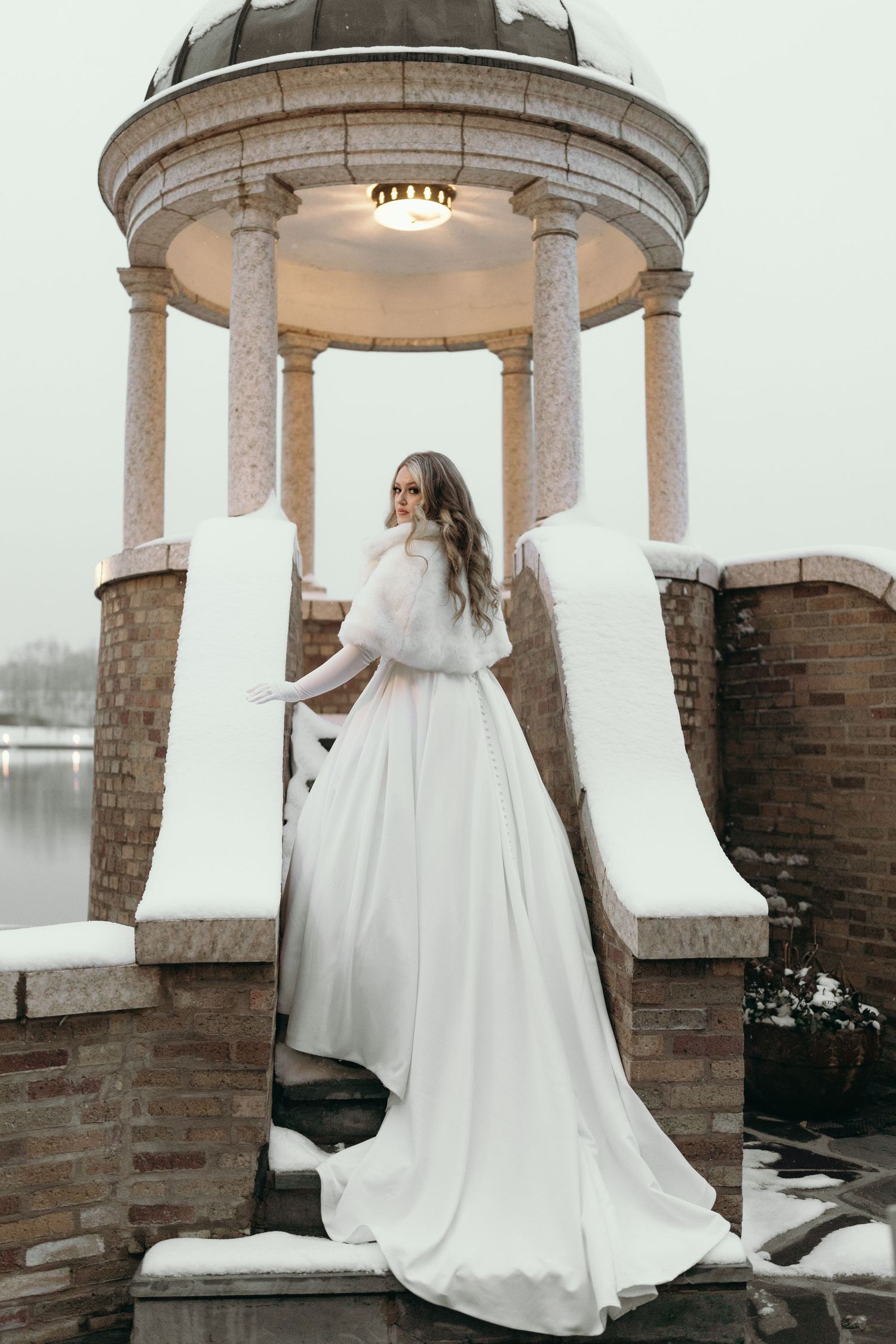Snow-covered gazebo provides elegant backdrop for winter bridal portrait.