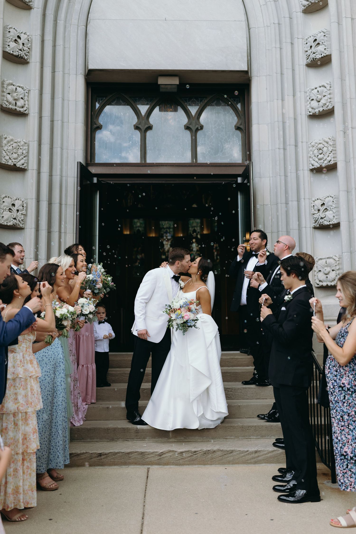 Wedding guests gather outside a grand stone church entrance during a celebration.