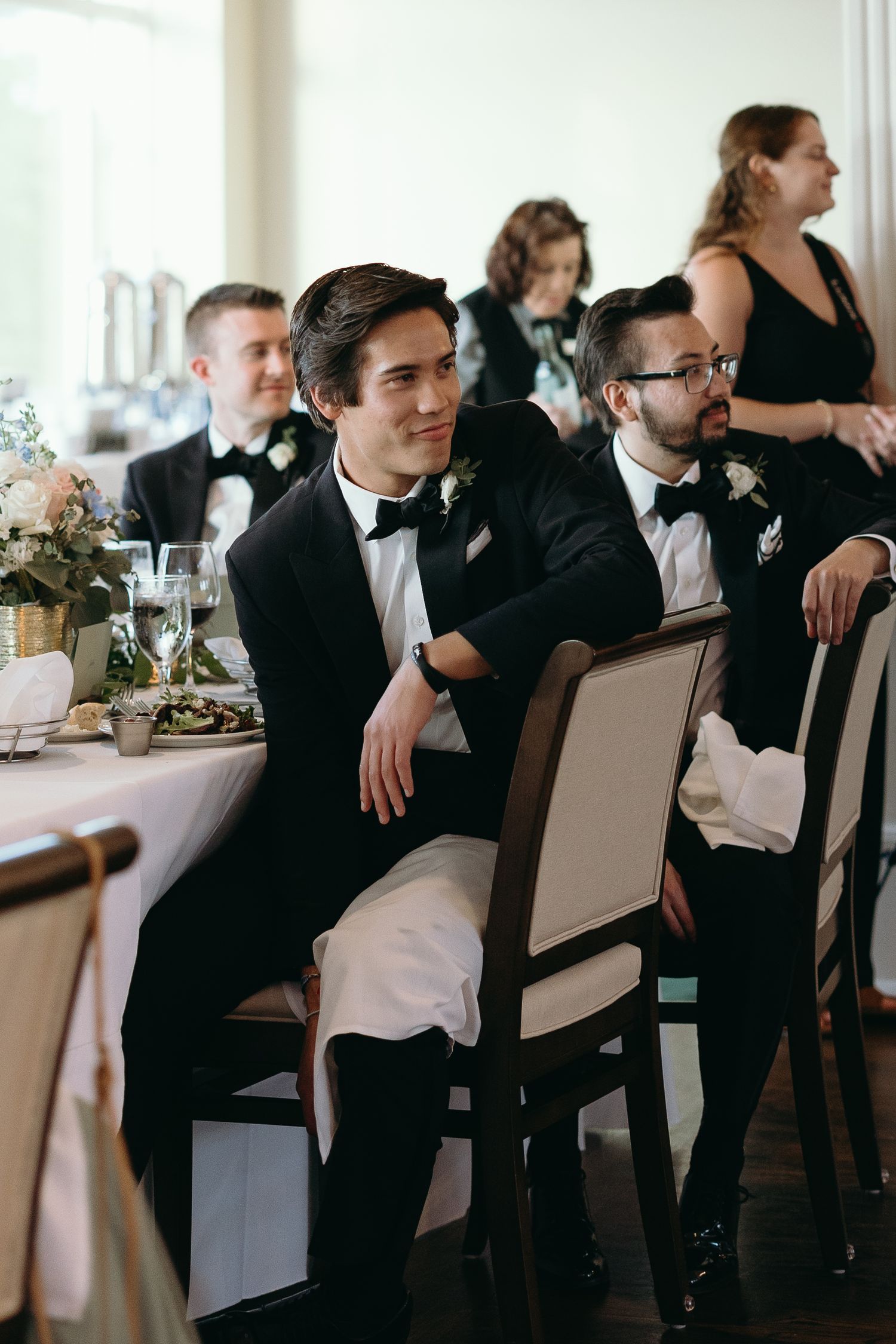 Groomsmen in tuxedos seated at elegant reception table.