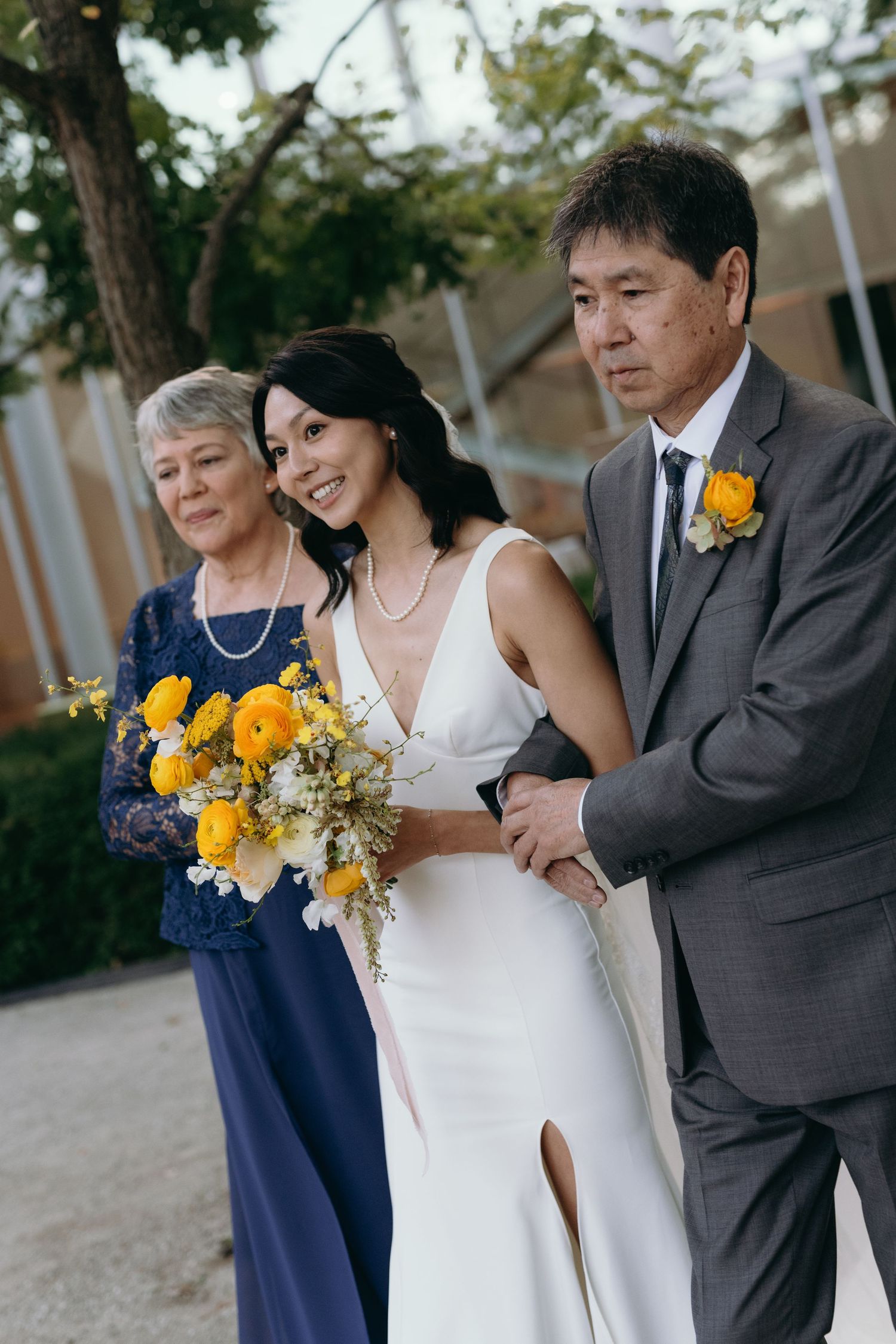 A wedding party poses together with bright yellow floral bouquets against an outdoor backdrop.