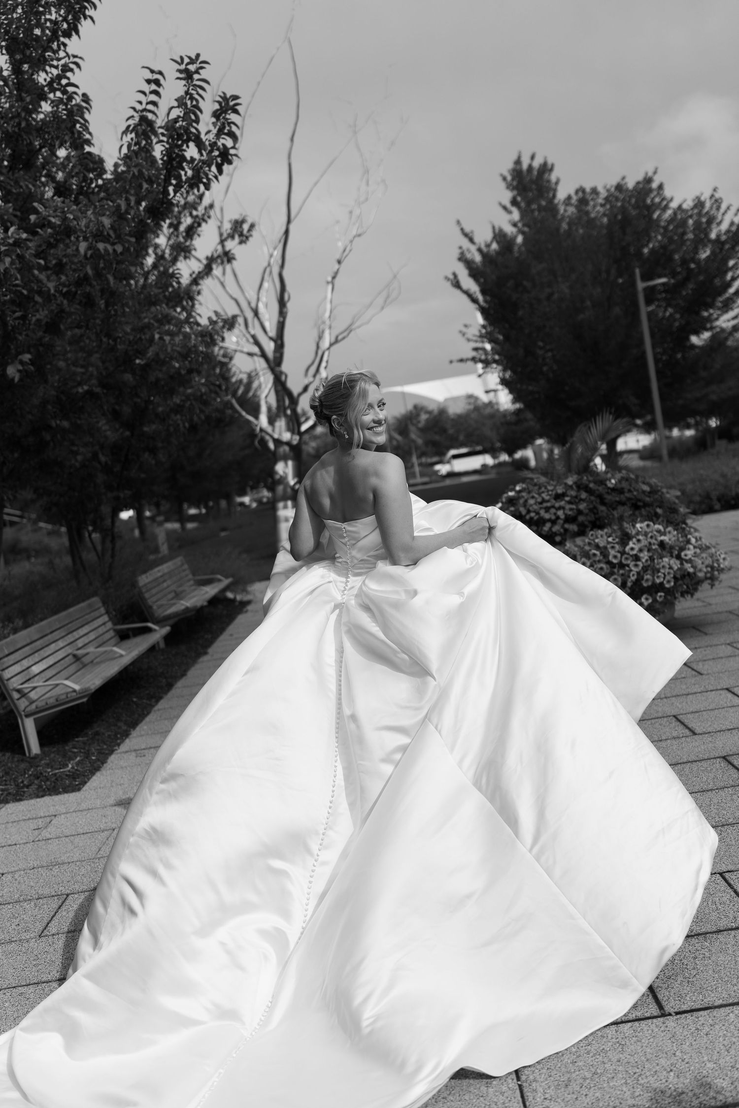 A series of black and white photos capturing a bride's flowing white dress in motion against an outdoor garden setting.