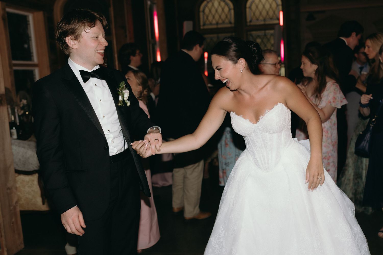 Joyful bride and groom dancing together at wedding reception in elegant gothic-style ballroom.