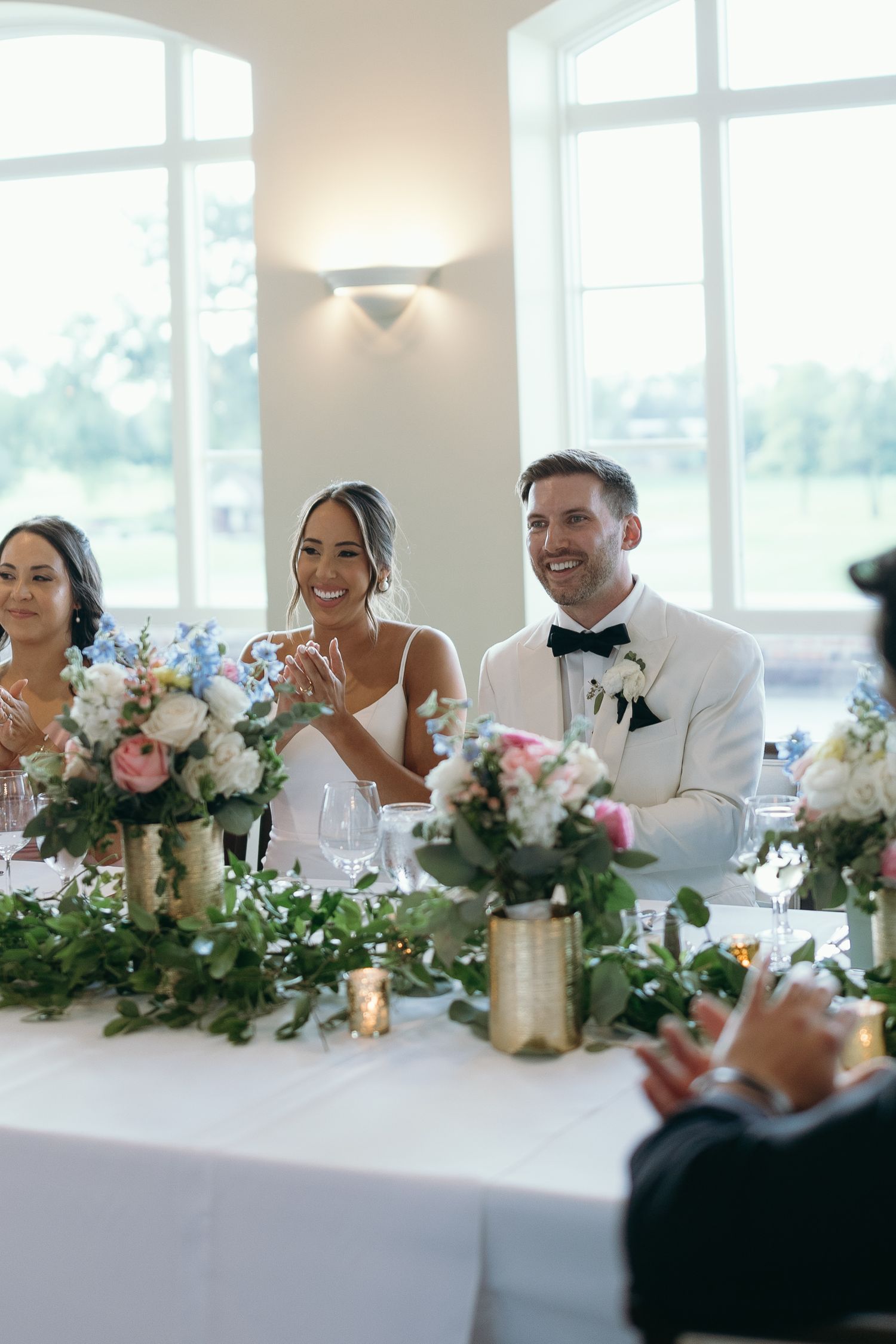 Wedding party seated at head table with elegant floral arrangements and candlelight.