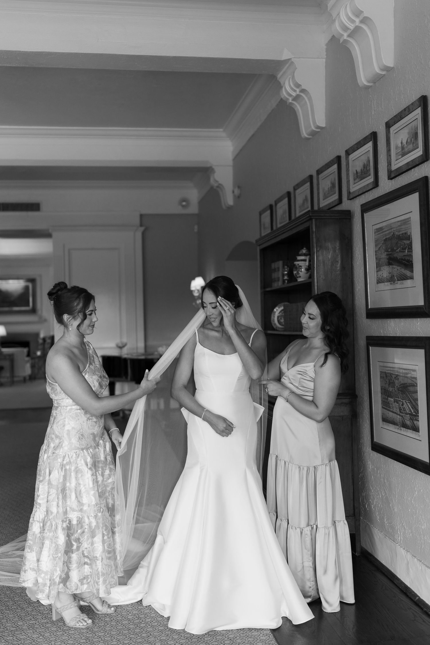 Bridesmaids in pastel dresses helping with wedding preparations in a hallway.