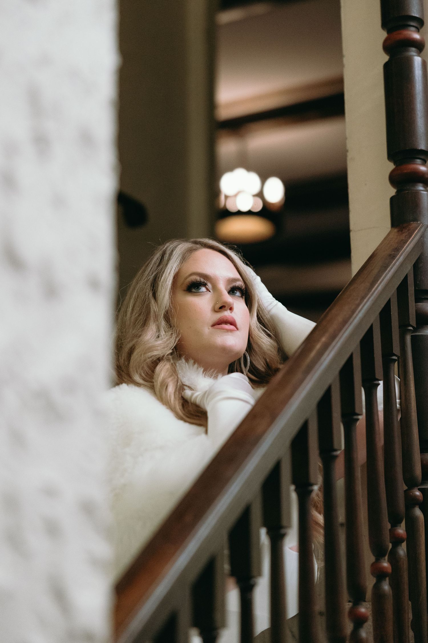 Elegant winter bride poses on vintage wooden staircase.