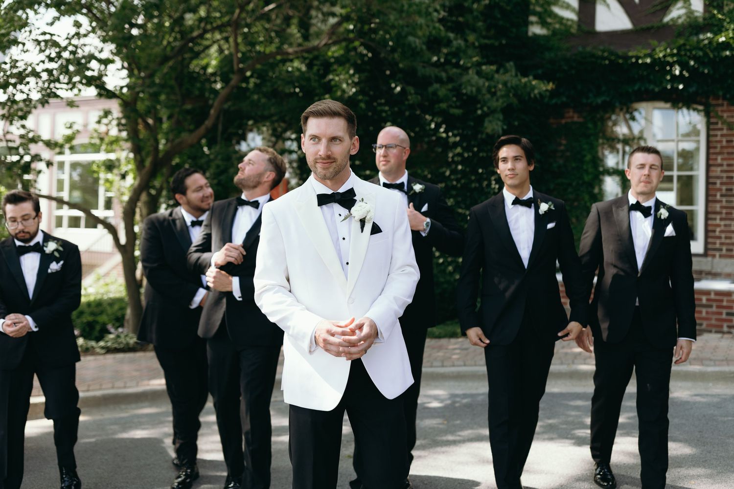 Groomsmen in black tuxedos stand behind groom in white dinner jacket.