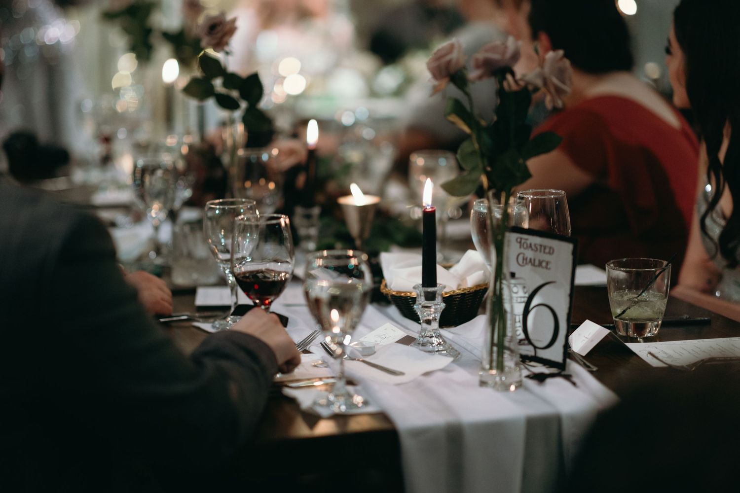 Elegant wedding reception table setting with wine glasses, candles and table number in moody lighting.