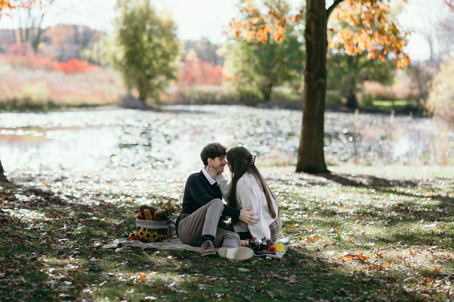 Intimate autumn scene of couple sitting by pond surrounded by fallen leaves.