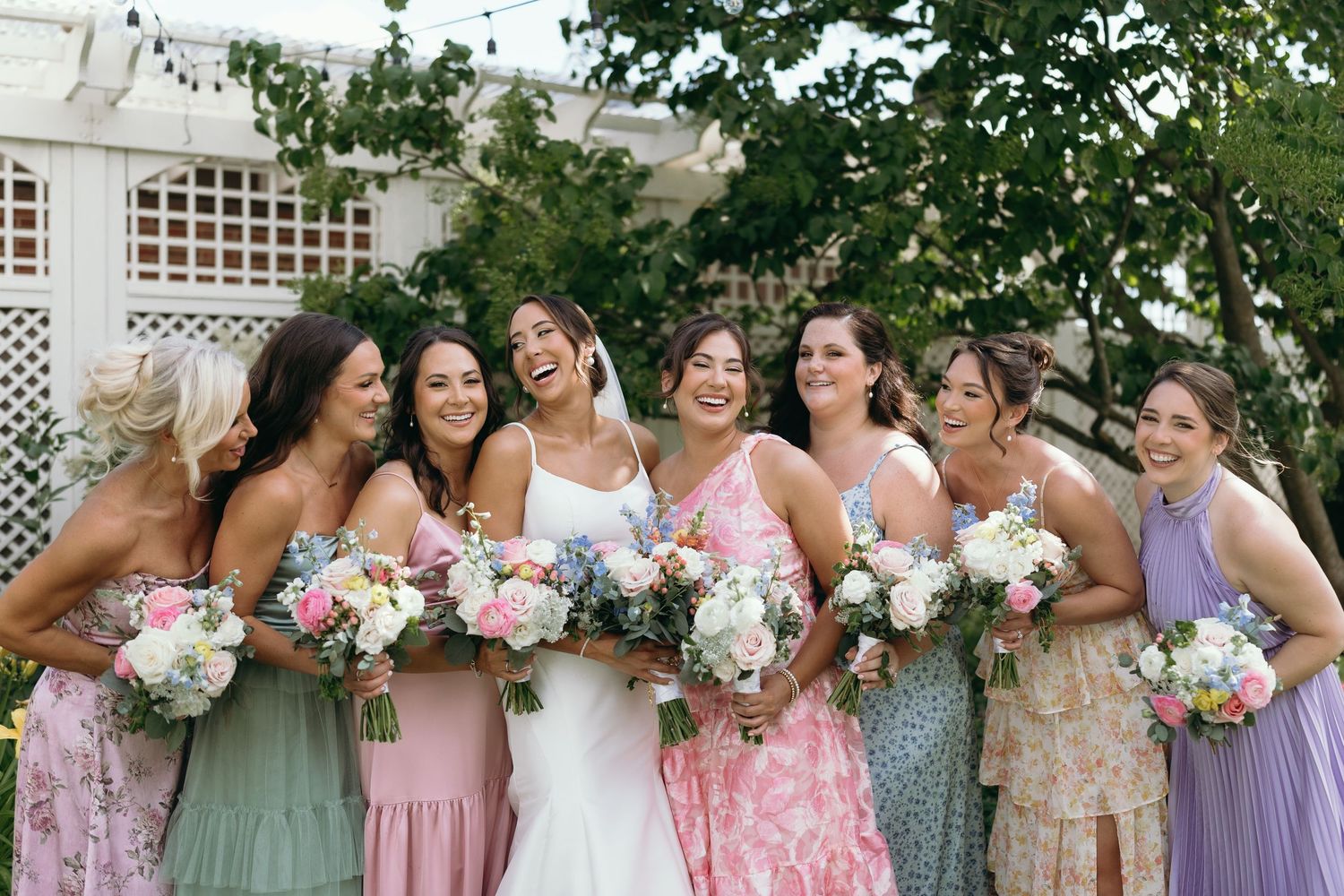 Bridesmaids in pastel floral dresses pose together at an outdoor wedding.