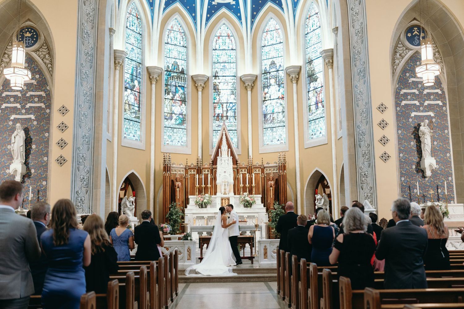 Traditional Catholic church wedding ceremony taking place in a beautiful Gothic cathedral with stained glass windows and vaulted ceilings.