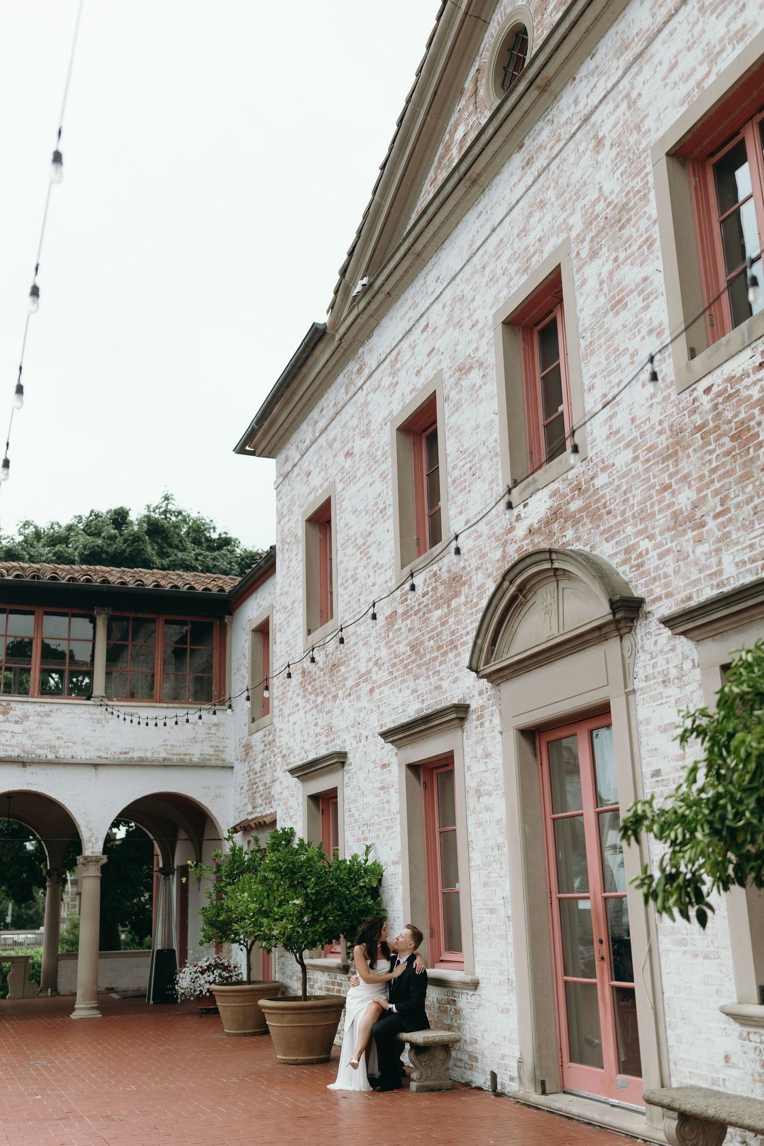 White stone building facade with arched doorways and string lights creates an elegant outdoor gallery setting at a venue.