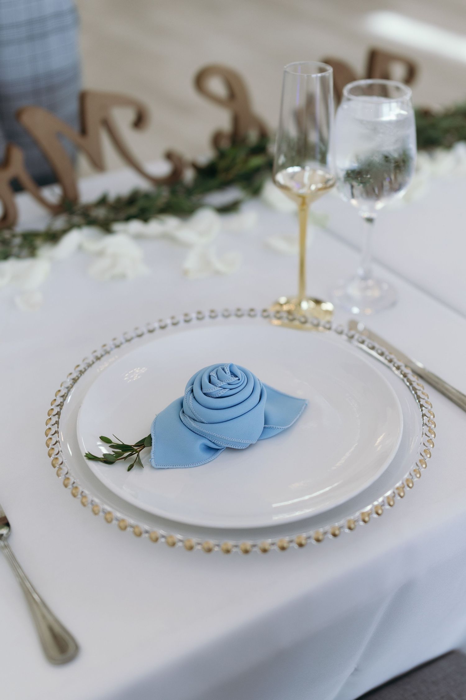 Place setting with beaded charger plate and blue rose napkin fold at wedding reception.