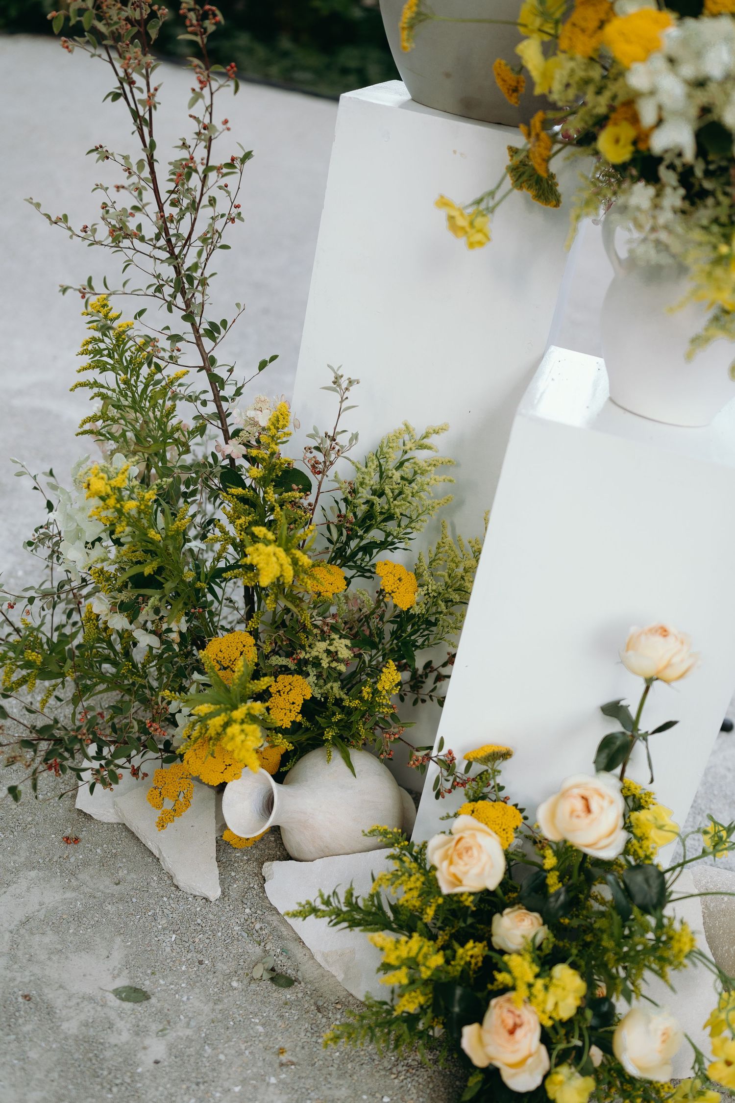 Delicate floral arrangements in yellow and peach tones decorating white wedding ceremony elements.