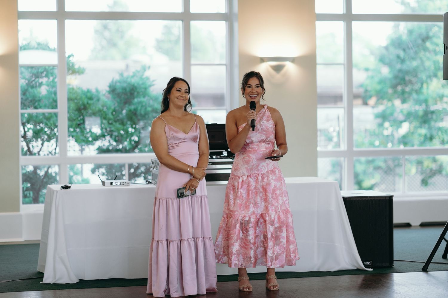Two attendees in pink dresses giving speeches at wedding reception.