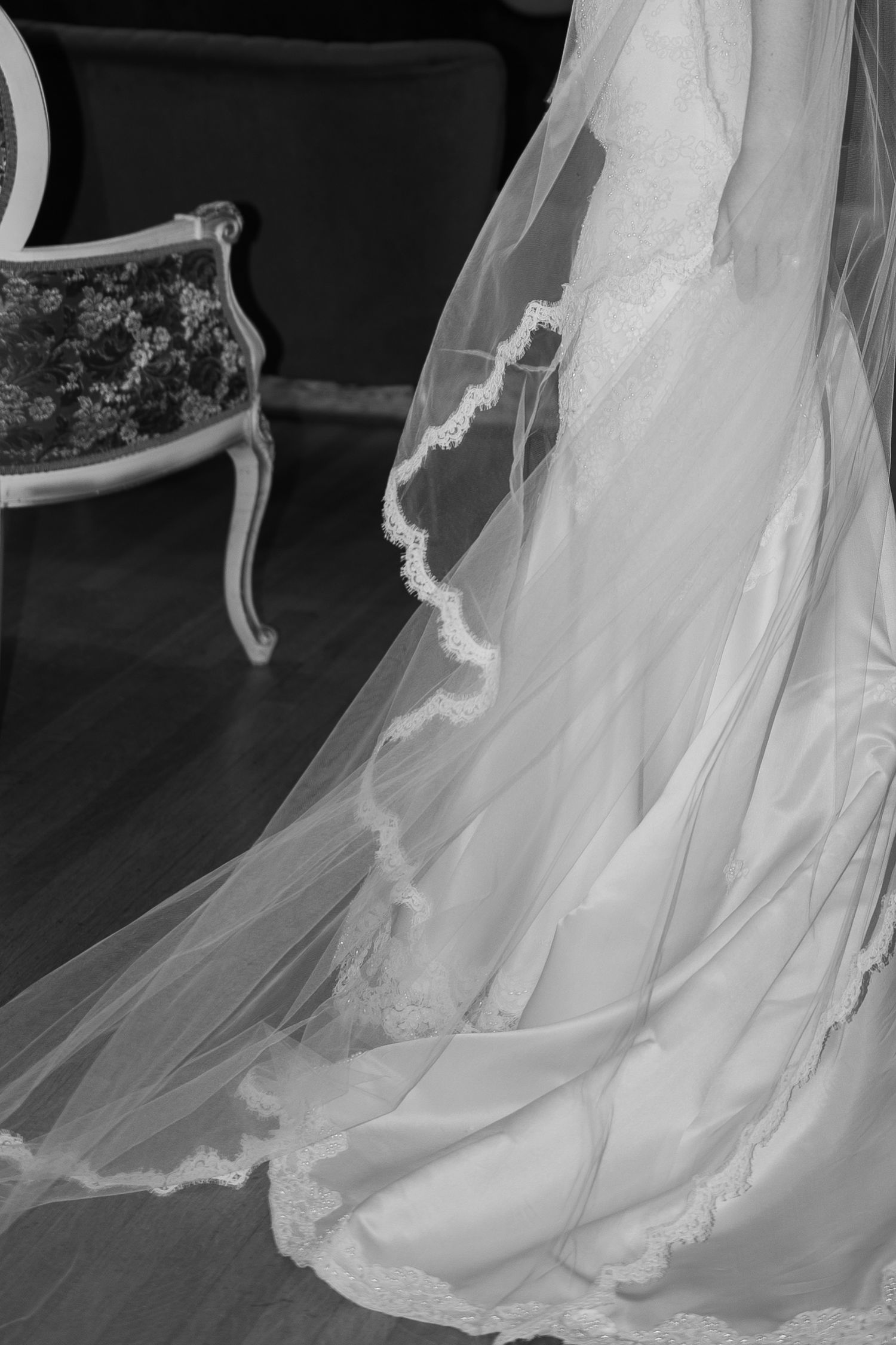 A flowing white wedding dress veil and train against a dark background with an ornate chair.