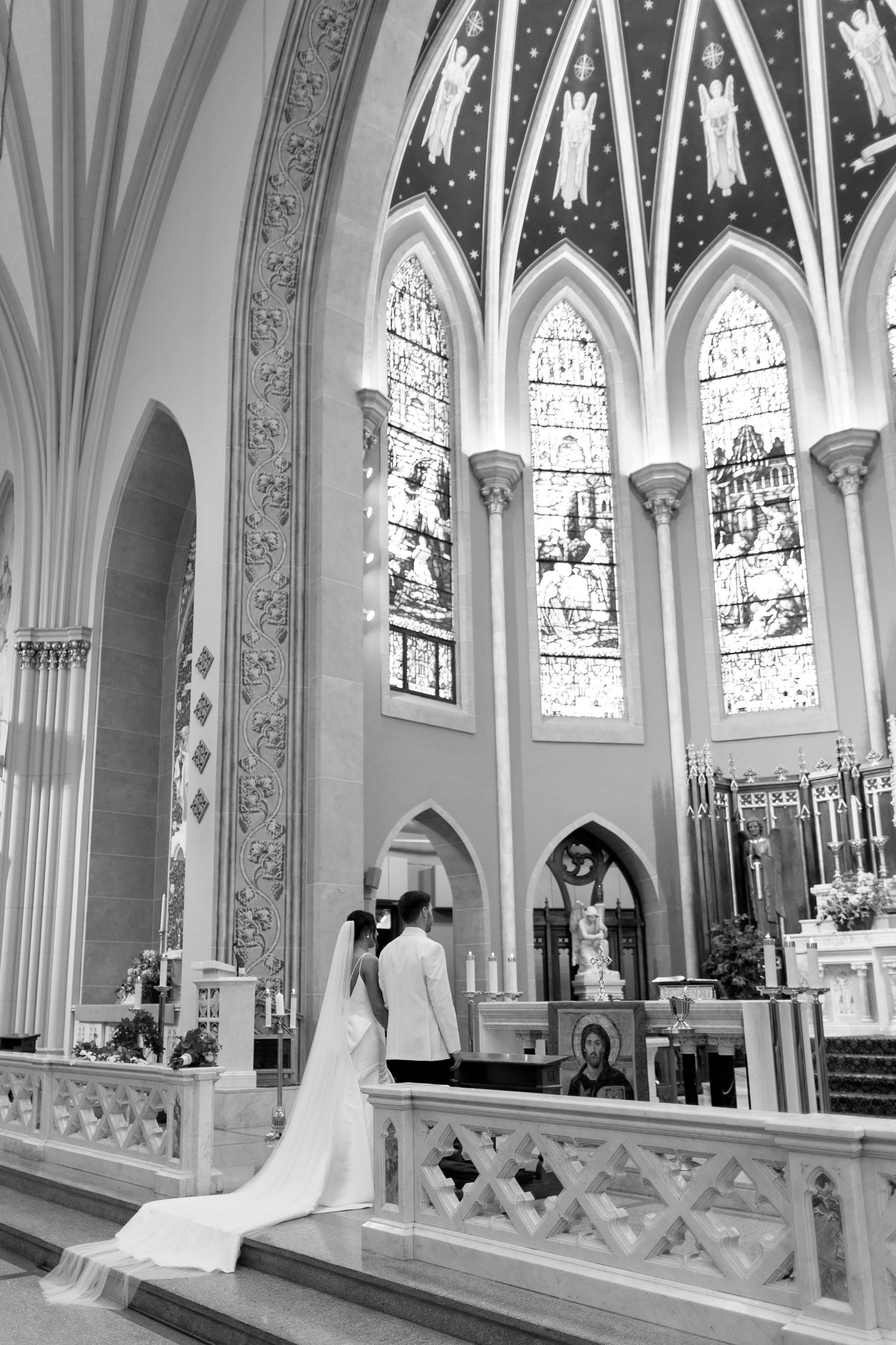Black and white photo of a wedding ceremony in a grand cathedral with stunning stained glass windows and gothic architecture.