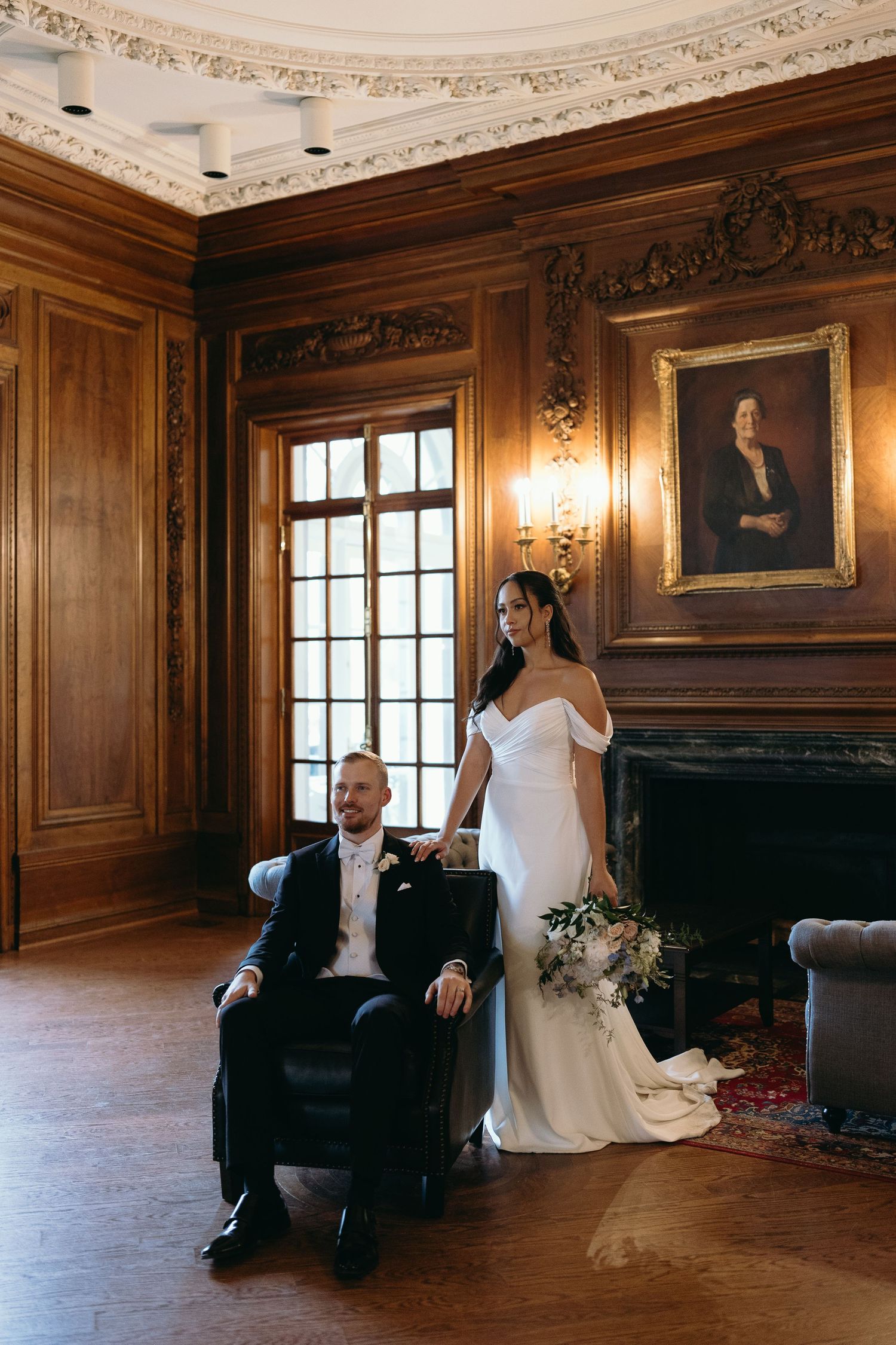 A wedding couple poses dramatically in a luxurious wood-paneled room with period furnishings.