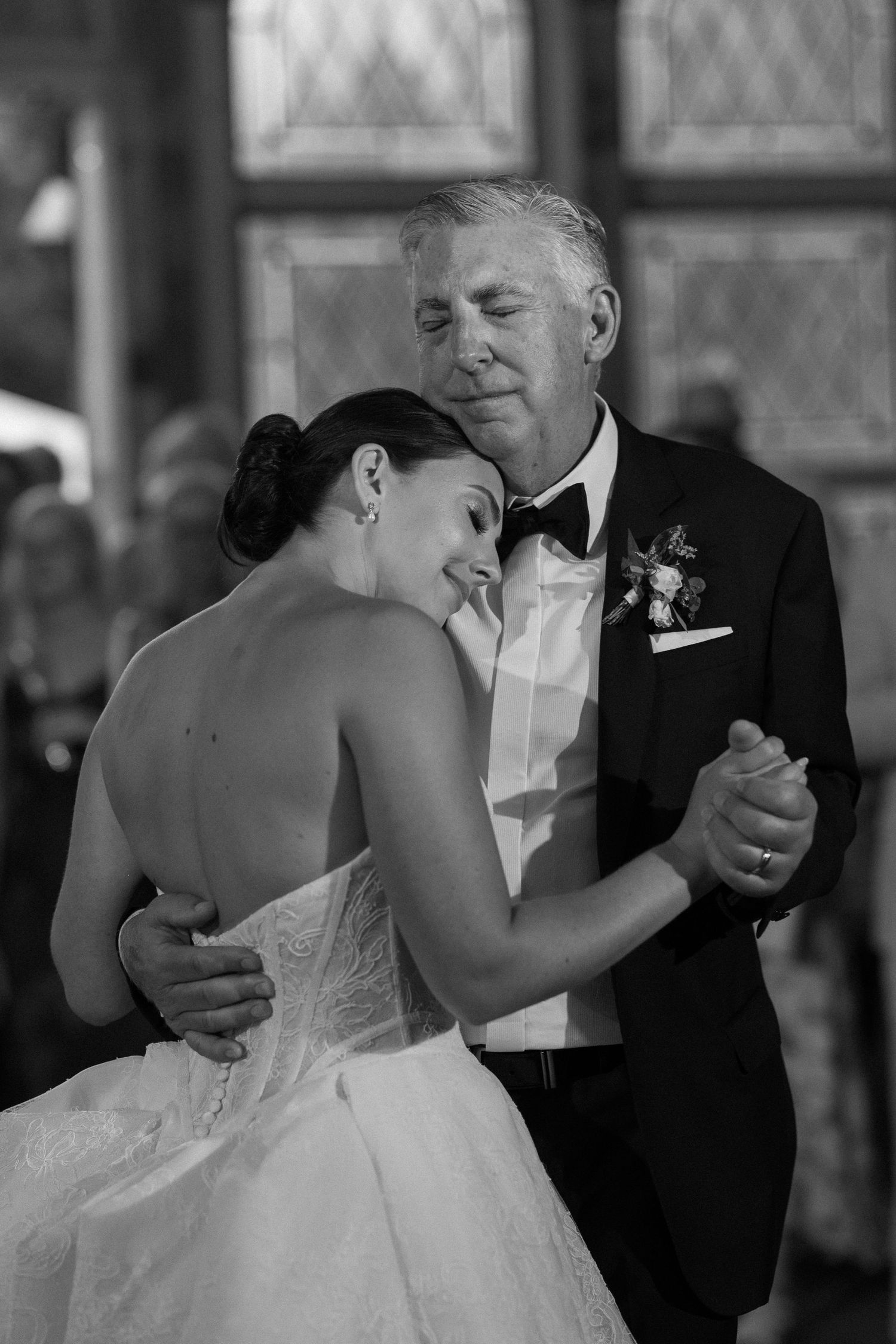 Black and white photo of bride resting head on fathers shoulder during emotional father-daughter dance.