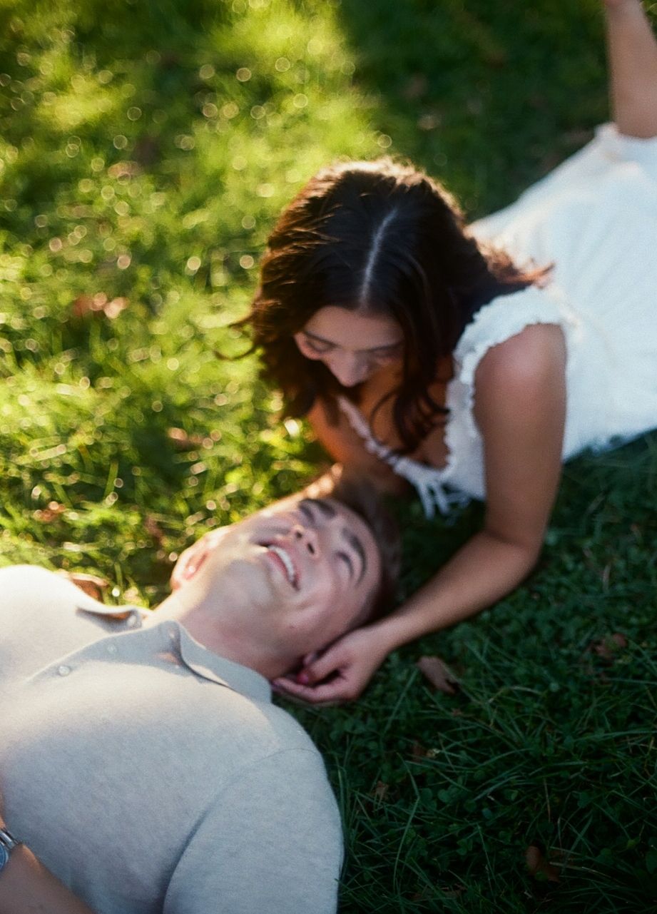 A romantic couple lying on green grass together in a dreamy summer setting, creating an intimate moment in nature.