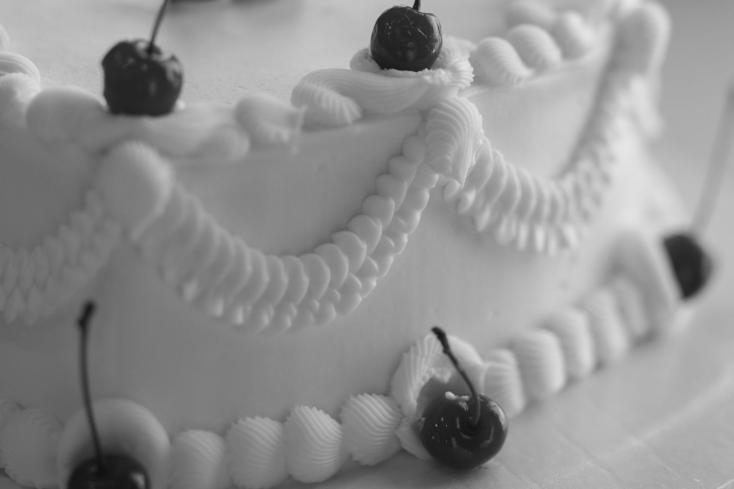 Closeup shot of a decorative white cake with fresh cherries and a string of pearls draped around its edges.