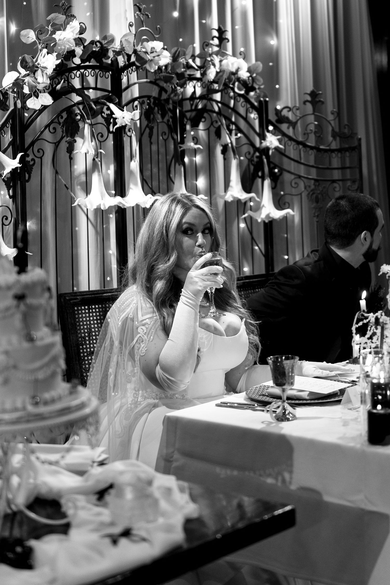 Black and white wedding reception photo with decorative lighting and table settings.