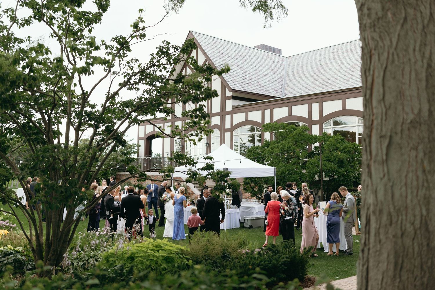 Wedding guests gather outside a grand white building for an outdoor reception.