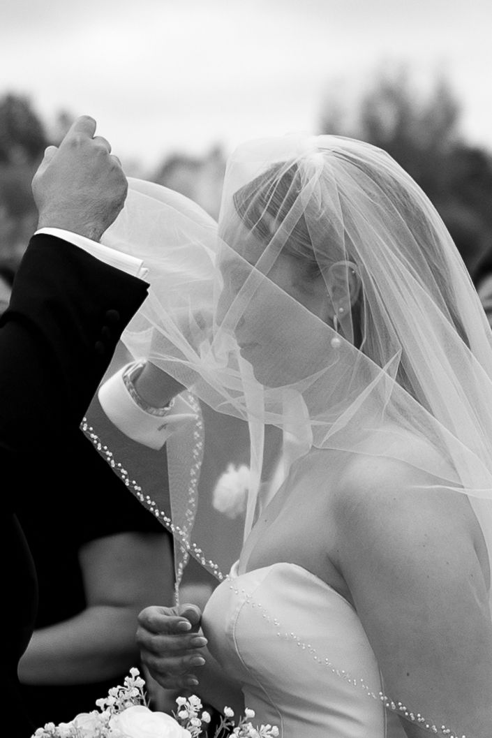 An intimate black and white moment captured through a delicate bridal veil.