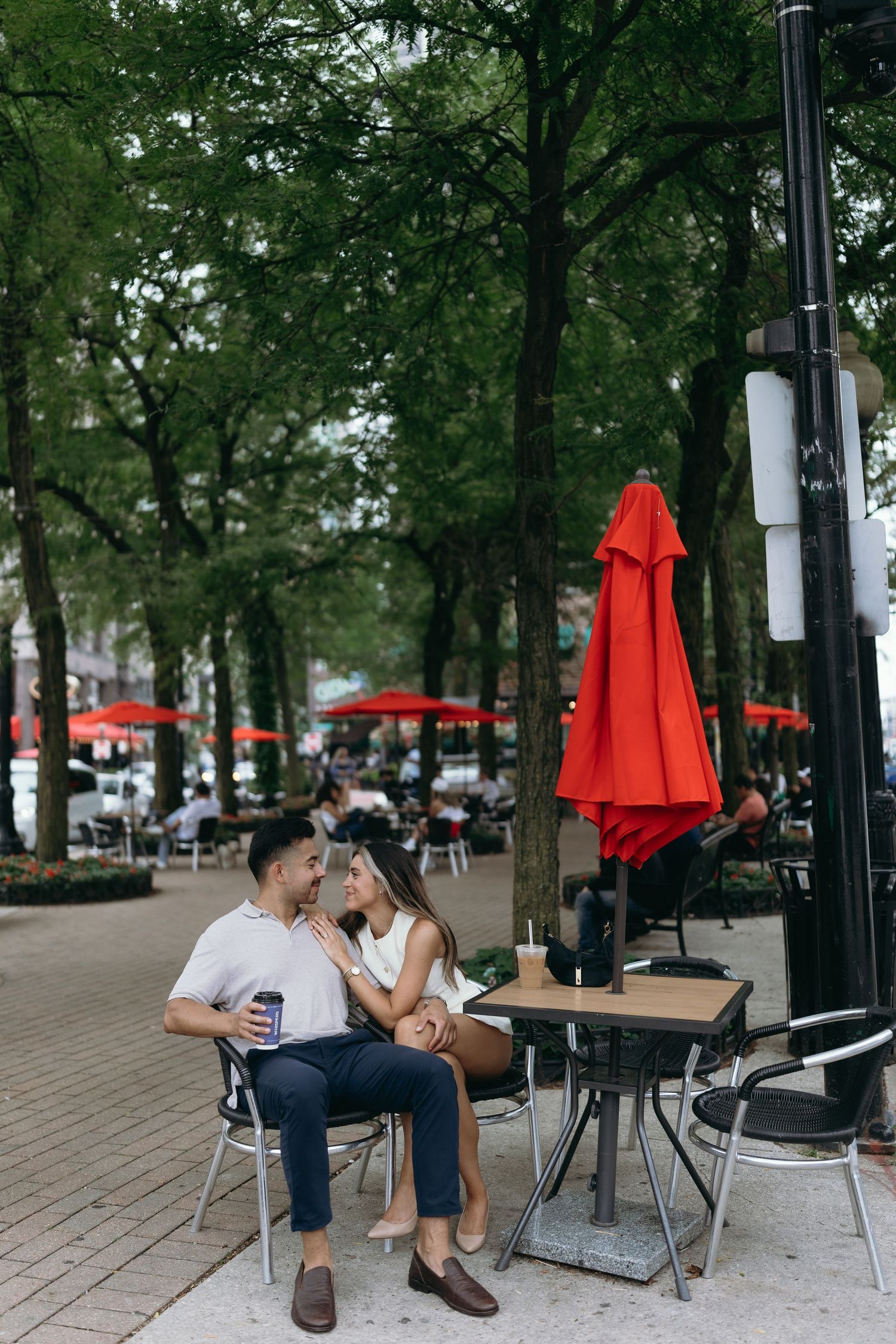 Three photos of an outdoor cafe seating area with red umbrellas and tables arranged under green trees on a brick patio.