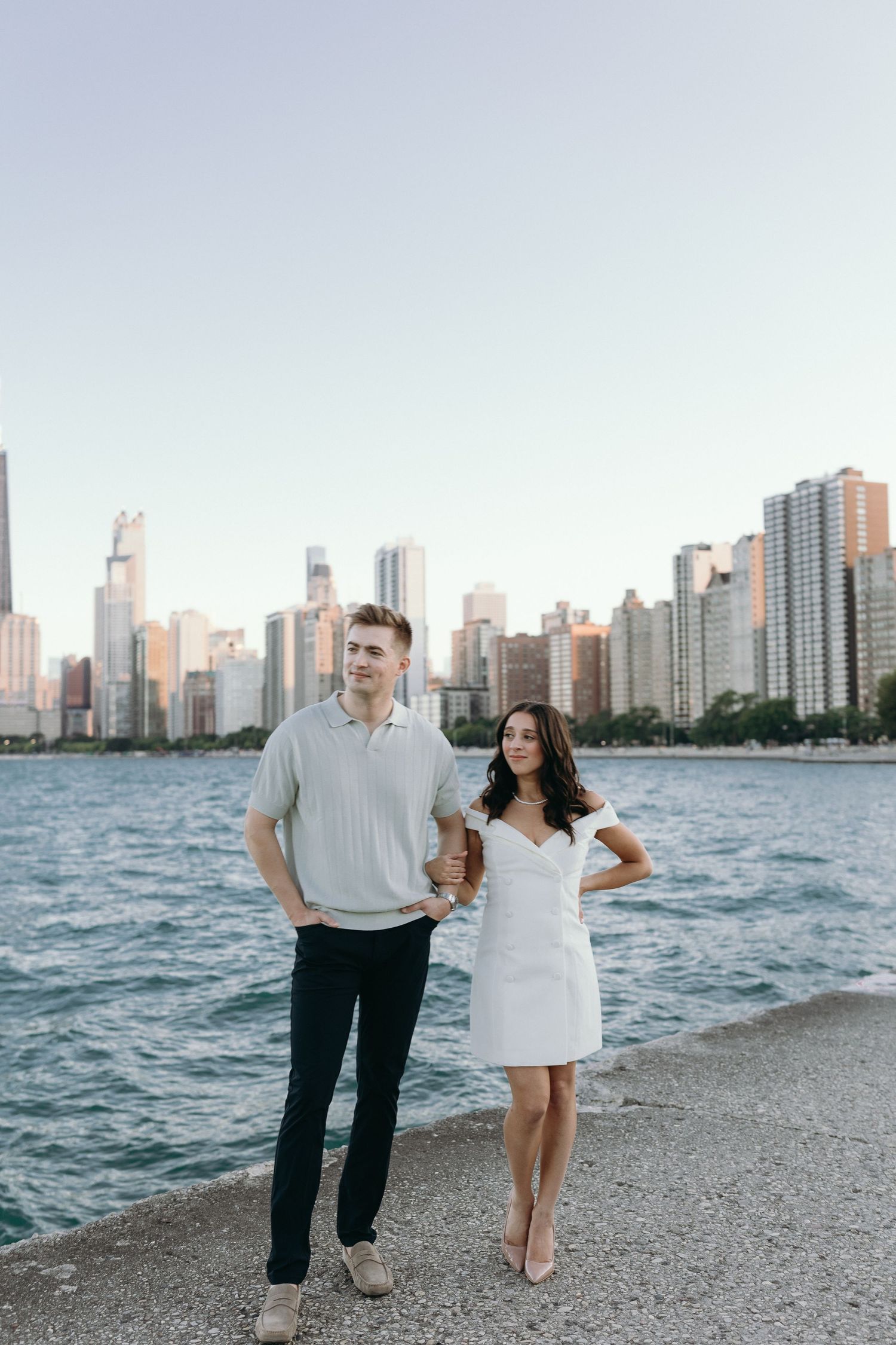 A couple walks along North Avenue Beach in Chicago with the city skyline and Lake Michigan in the background.