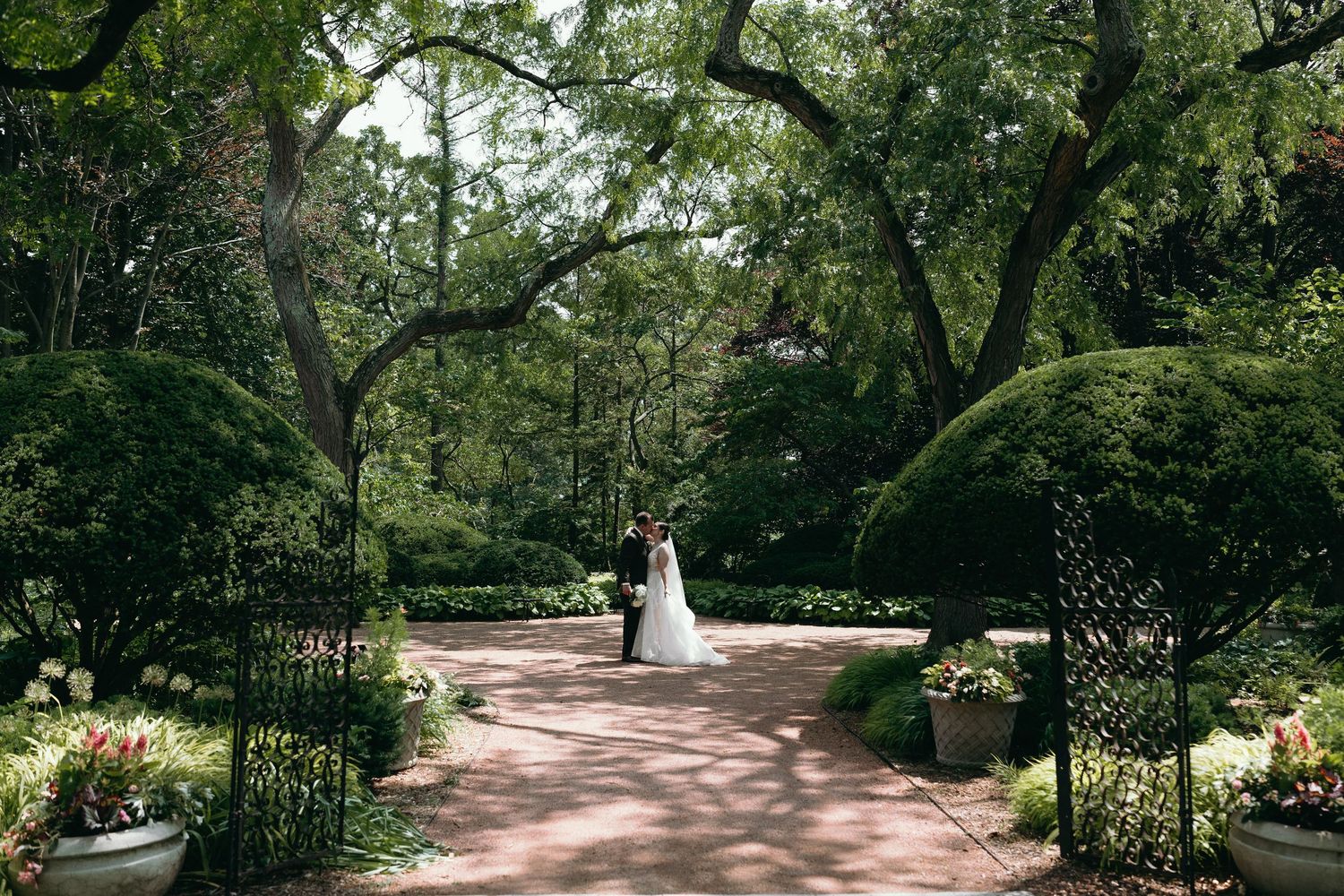 Garden wedding ceremony pathway lined with trees and floral arrangements.