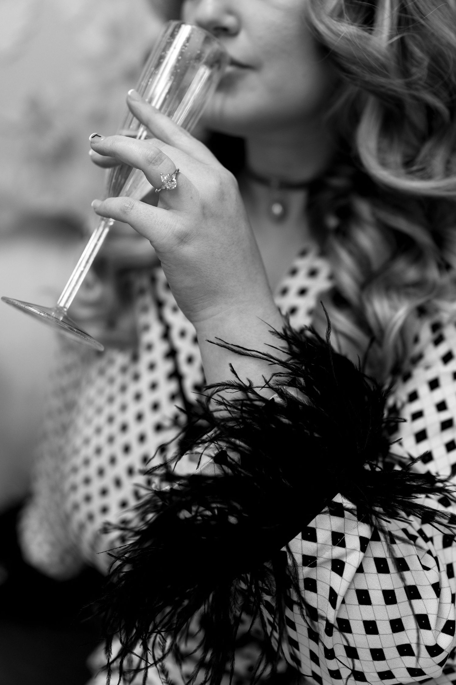 Elegant black and white photo of hand holding champagne glass with feather detail.