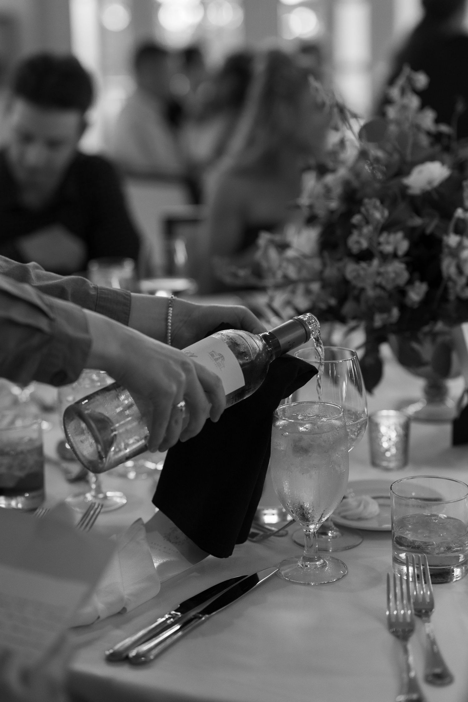 Black and white photo of someone pouring drinks at an elegant reception table.