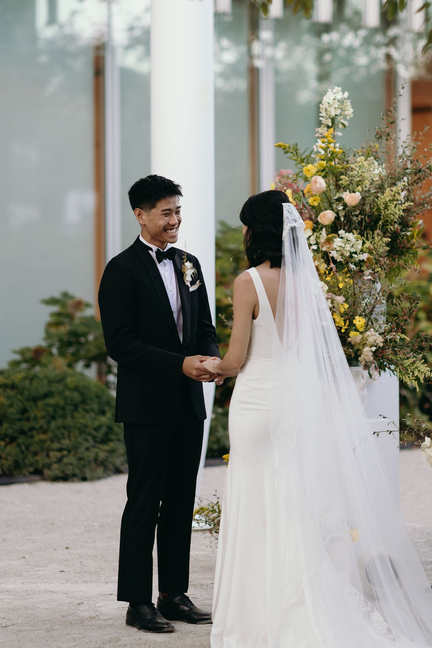 A couple shares a tender moment during their wedding ceremony beside yellow floral arrangements.