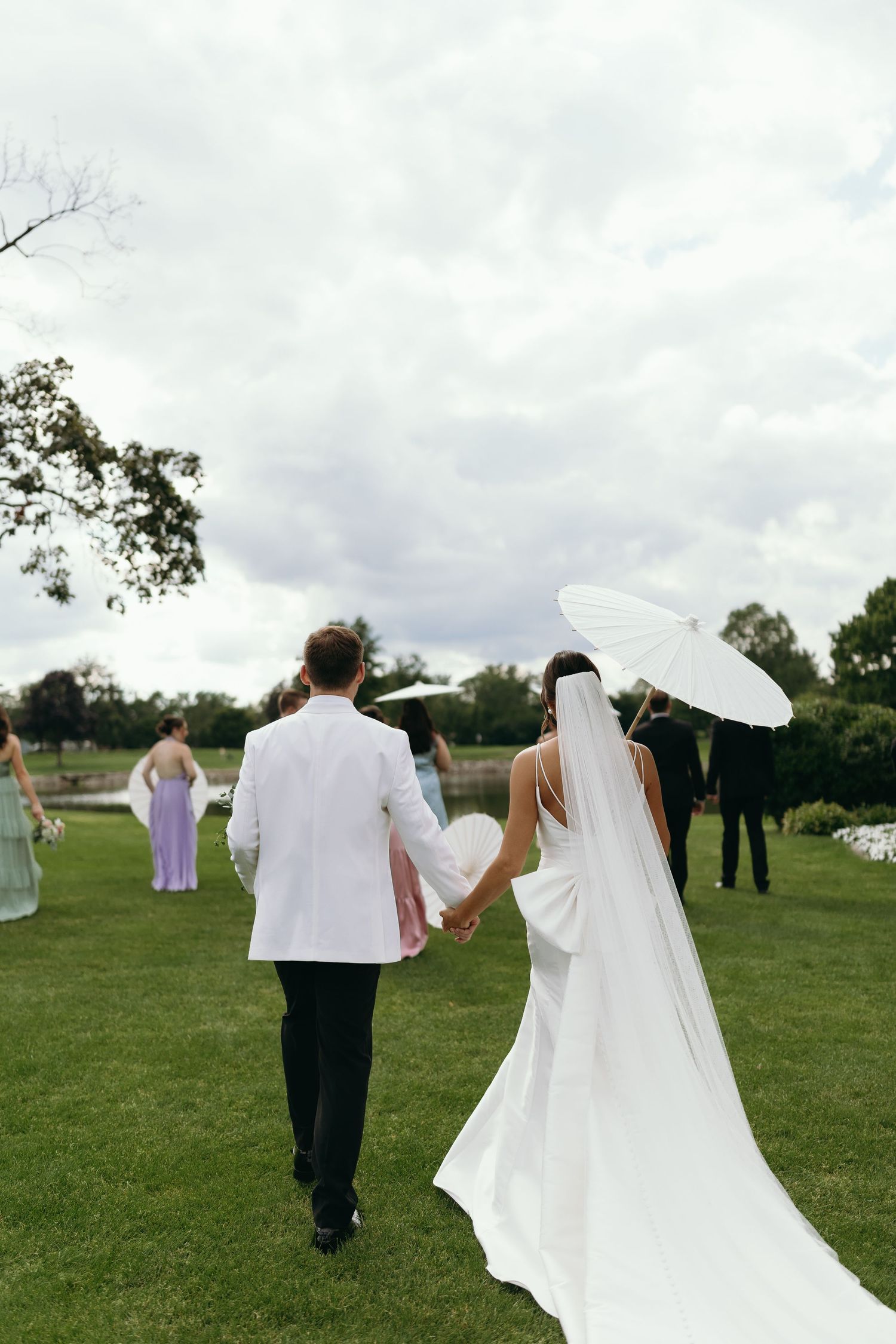 Wedding party walks across a grassy field under cloudy skies.