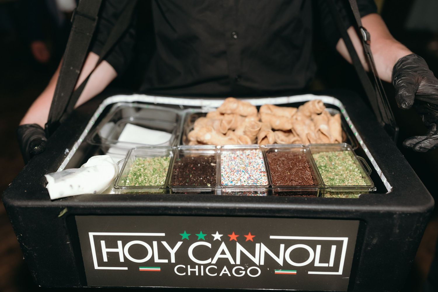 Holy Cannoli Chicago dessert station with assorted toppings and fillings displayed in a portable black cart.
