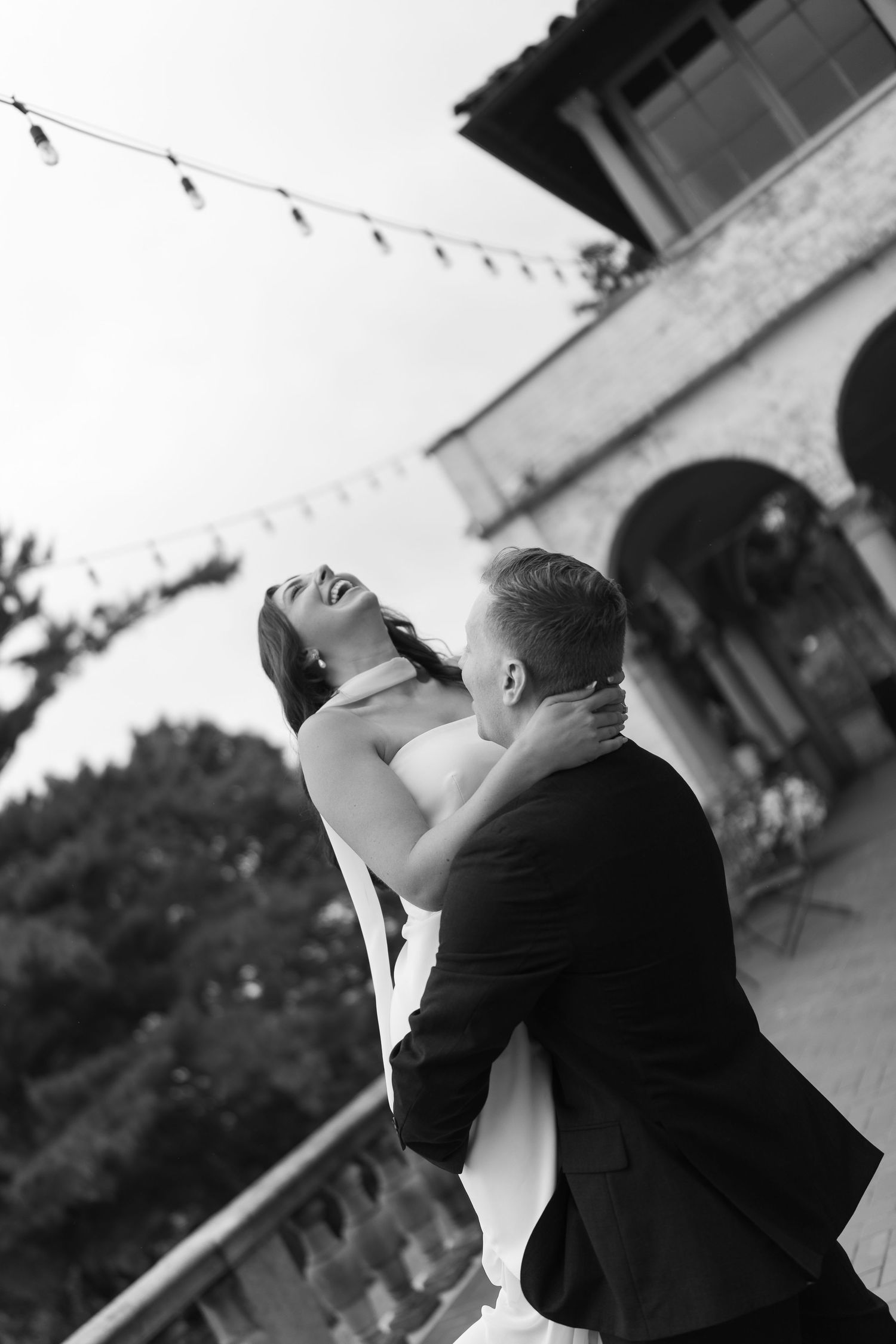 Black and white photograph of joyful dancing moment under string lights.