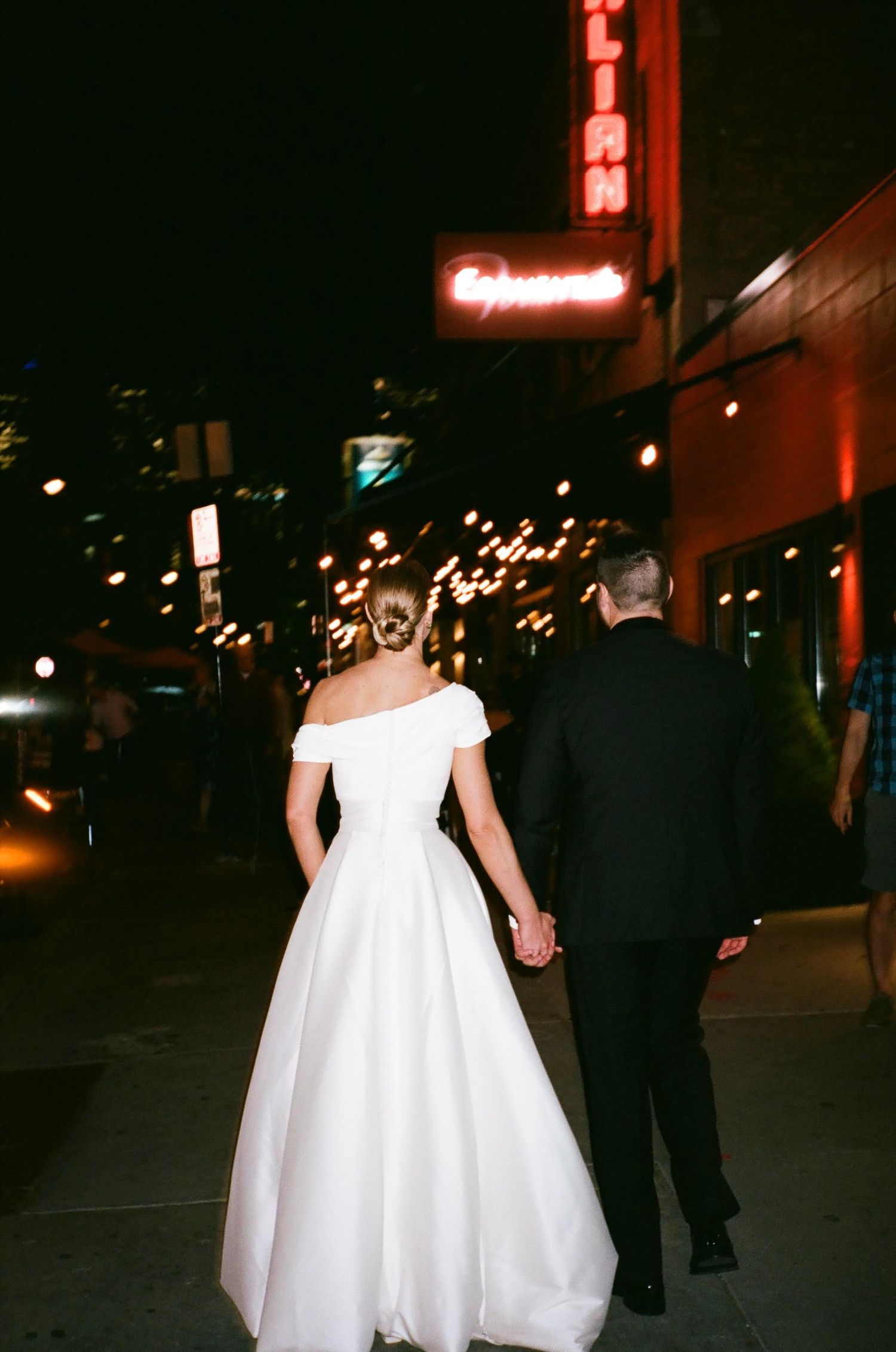 Couple walking hand in hand at night with neon signs and city lights.