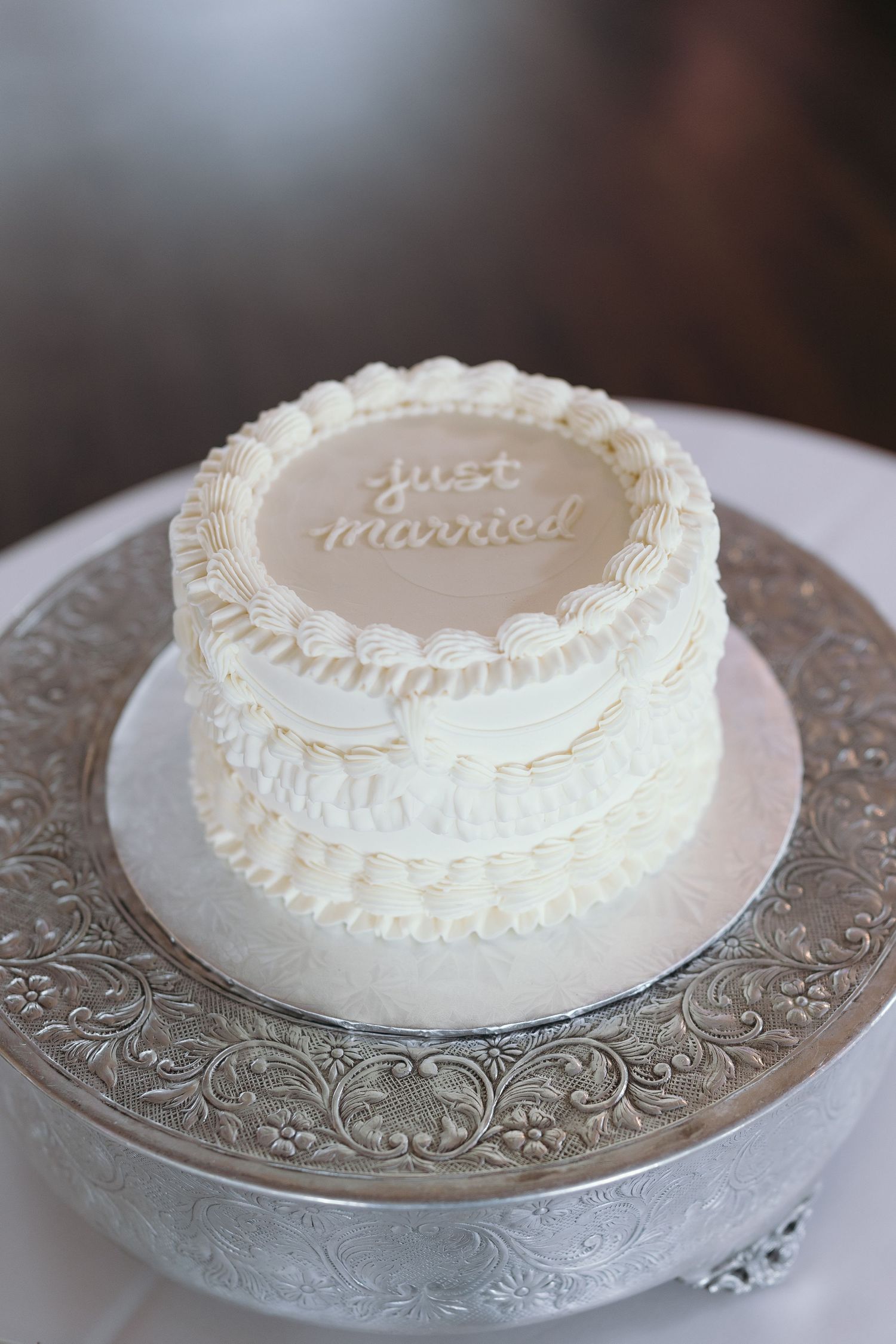 White wedding cake with 'Just Married' text and piped decorations on a silver cake stand.