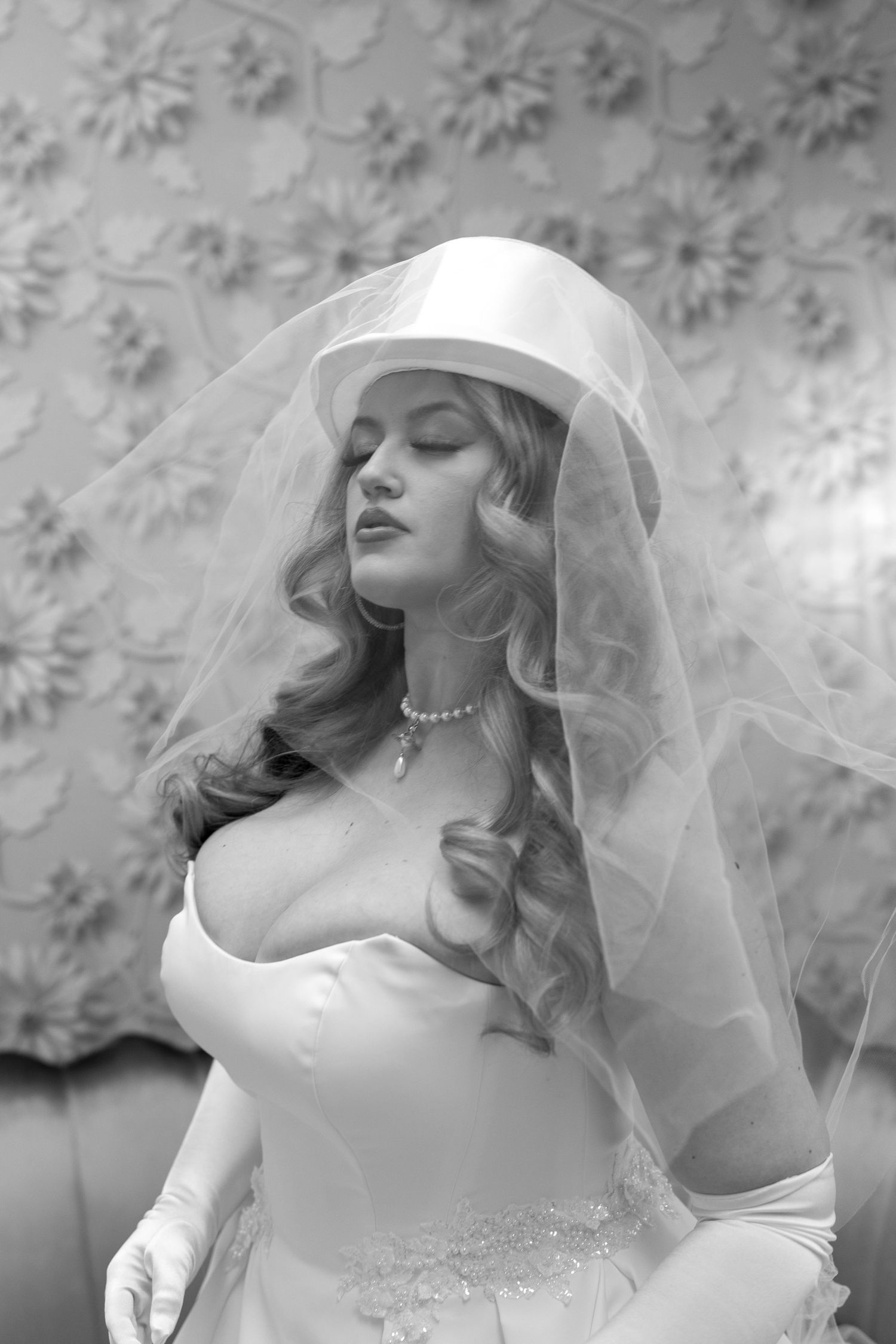 A vintage-style bridal portrait featuring a delicate veil and pearl necklace.